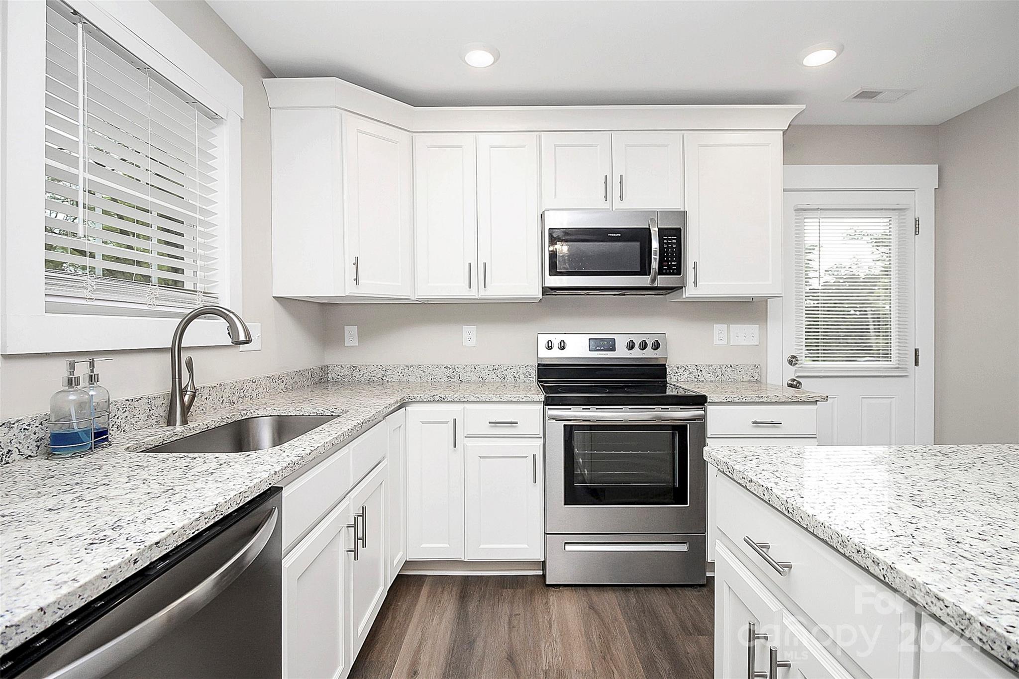 Bright kitchen with white cabinets, granite countertops, stainless steel appliances, and a window over the sink.