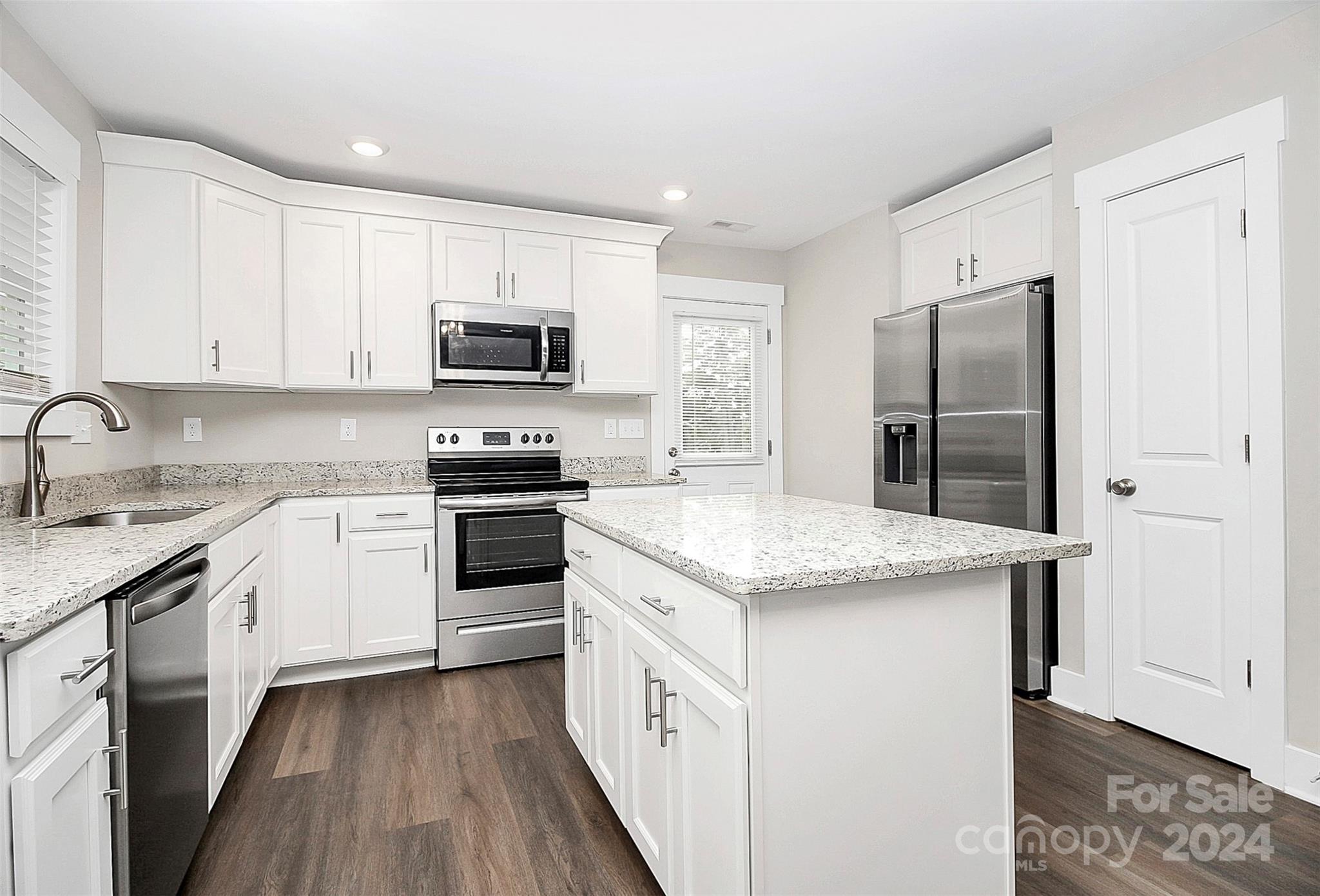 Bright kitchen with white cabinets, a large stone island, and stainless steel appliances.