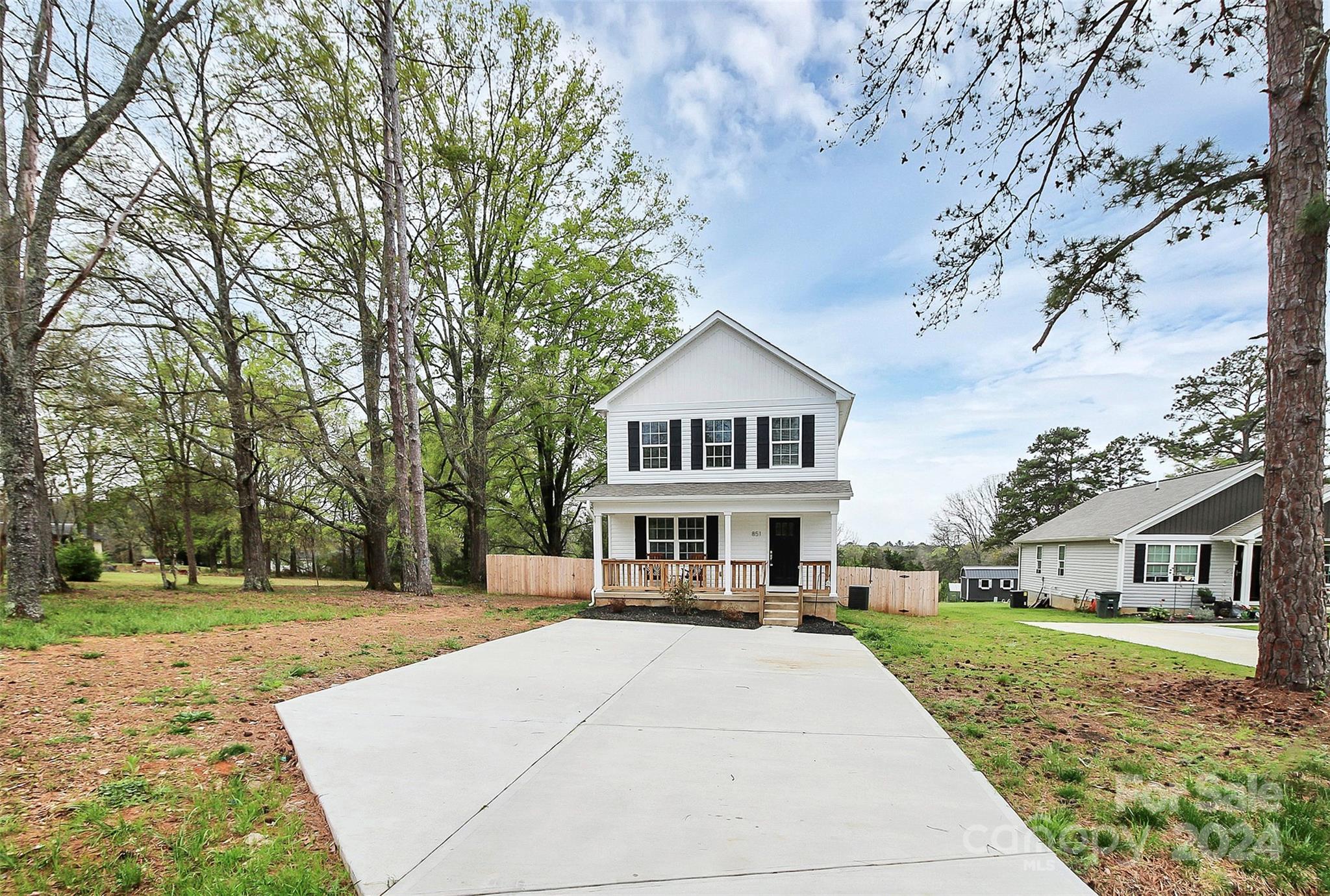 White two-story house with black shutters, a front porch, and a wide concrete driveway.