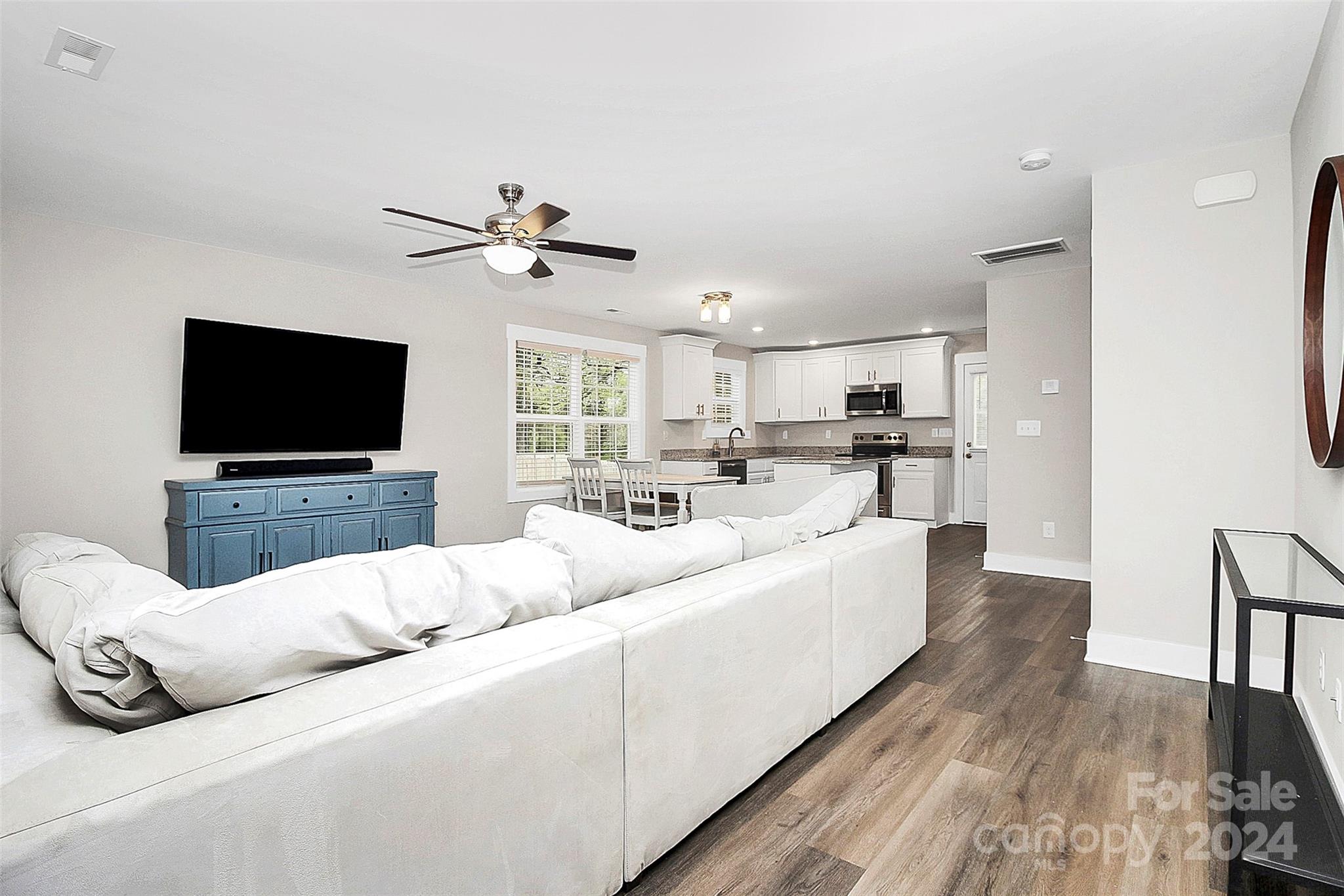 Open-plan living room with a large white sectional, blue TV console, and kitchen beyond.