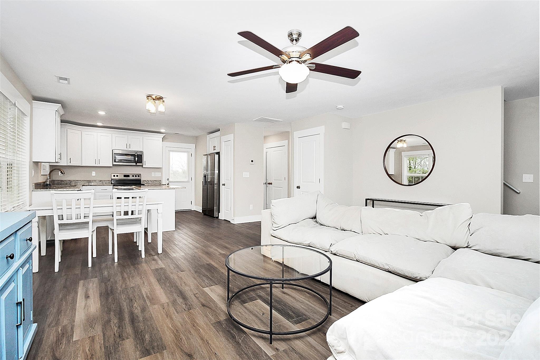 Open-plan living room and kitchen with a white sectional, glass coffee table, and white cabinetry.