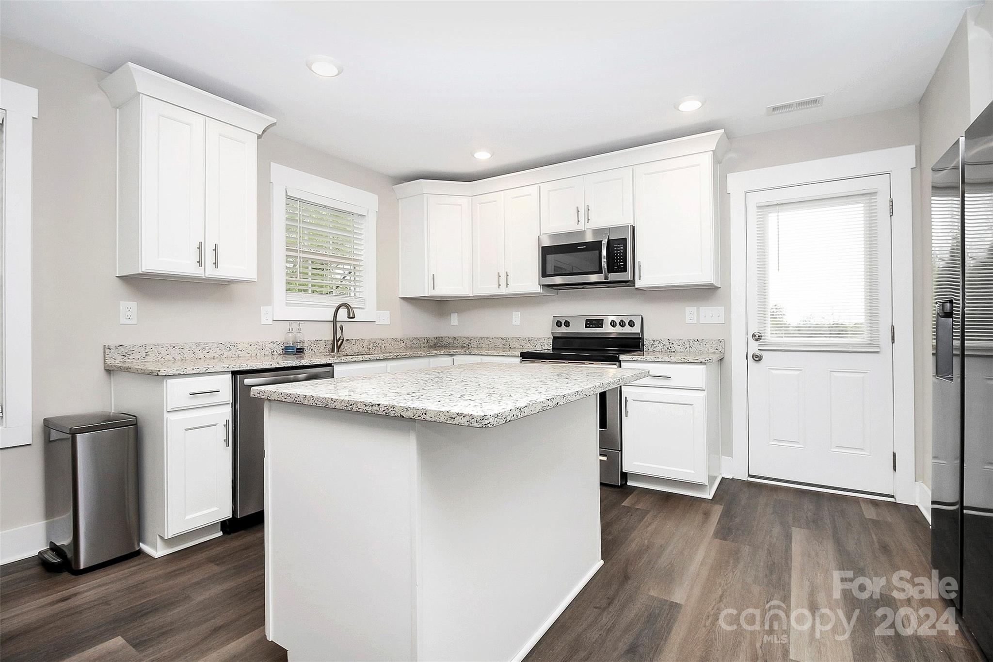 Kitchen with white cabinets, a large stone-topped island, stainless appliances, and dark flooring.