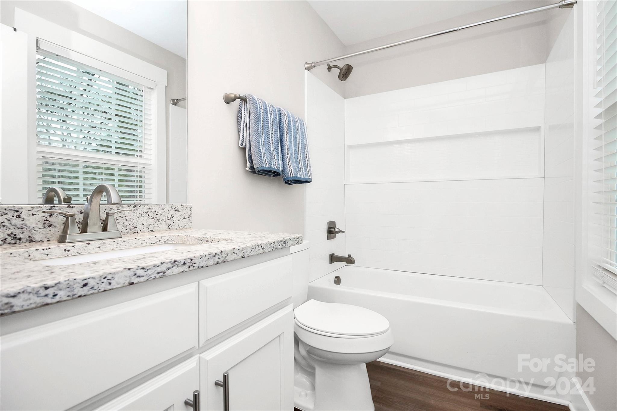 Bright bathroom with a granite vanity, white tiled tub and shower, and blue striped towels.