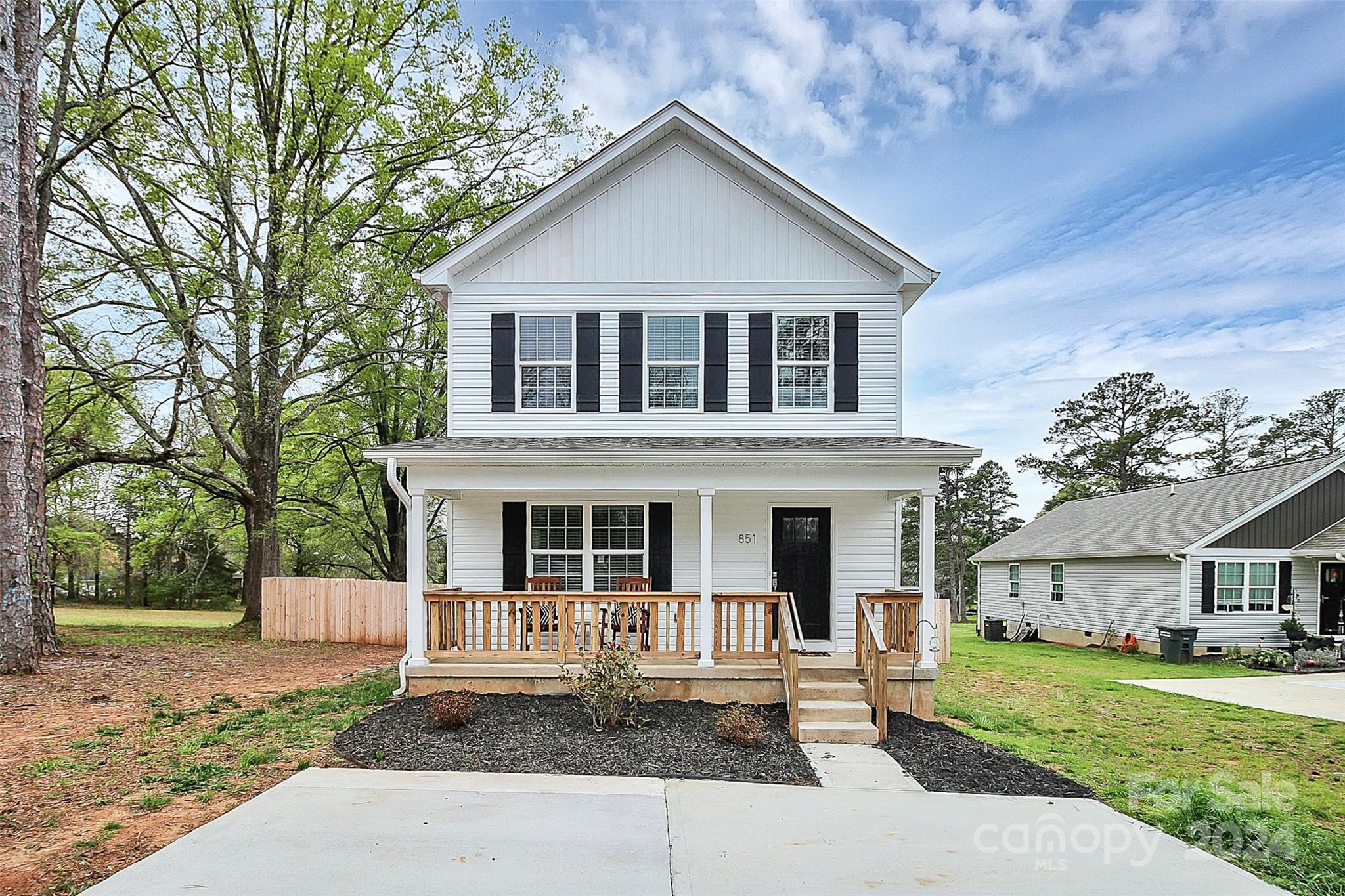 Two-story white house with black shutters, a covered wooden porch, and a concrete driveway.