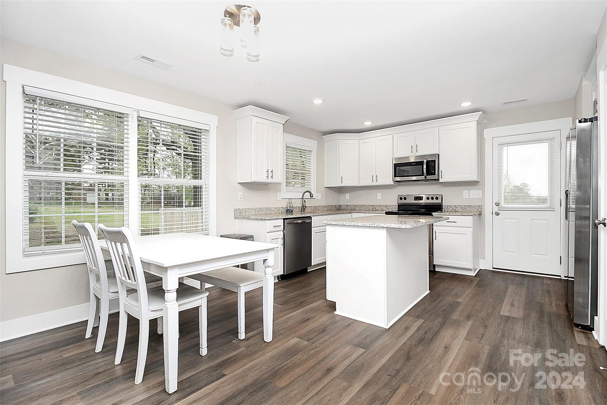 Bright kitchen with white cabinets, stainless steel appliances, granite counters, central island, and dining table by large windows.