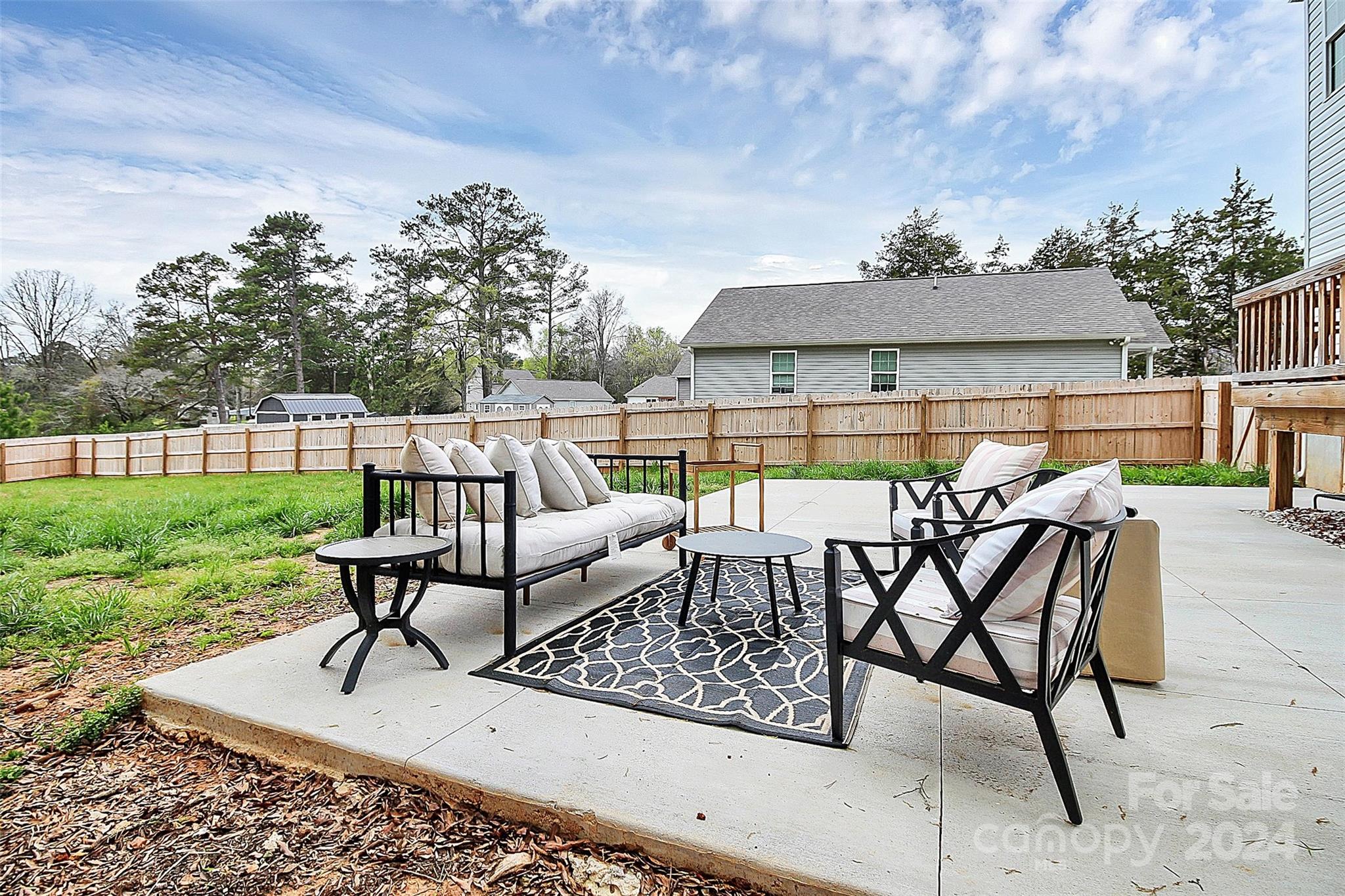 Furnished concrete patio with black seating, pale cushions, a patterned rug, and a fenced backyard.