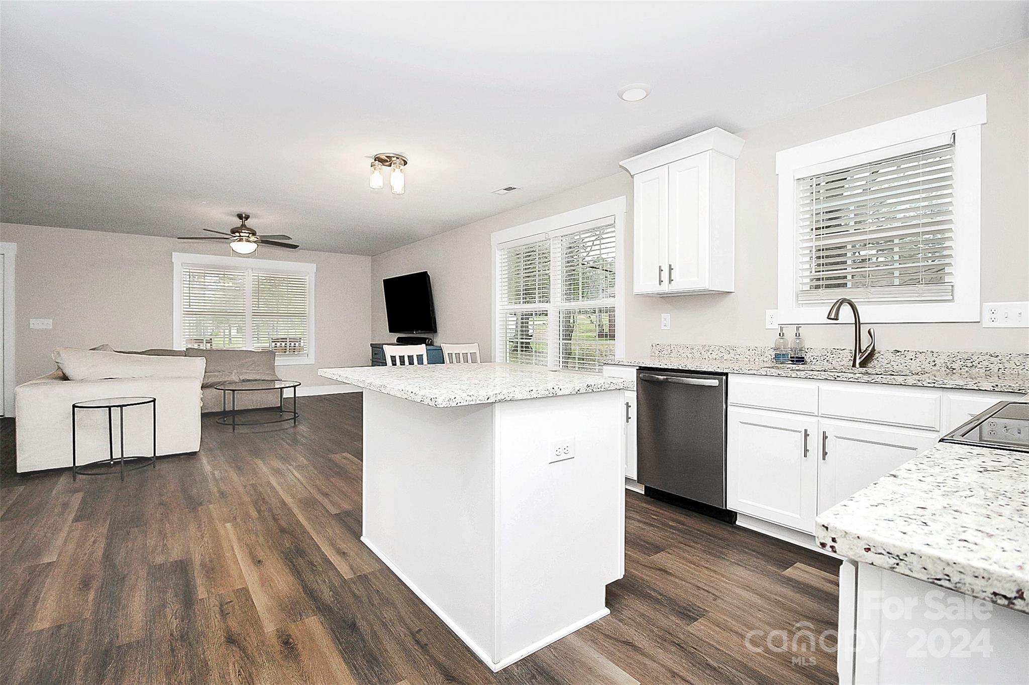 Open kitchen and living area with a large stone island, white cabinetry, and dark wood-look floors.
