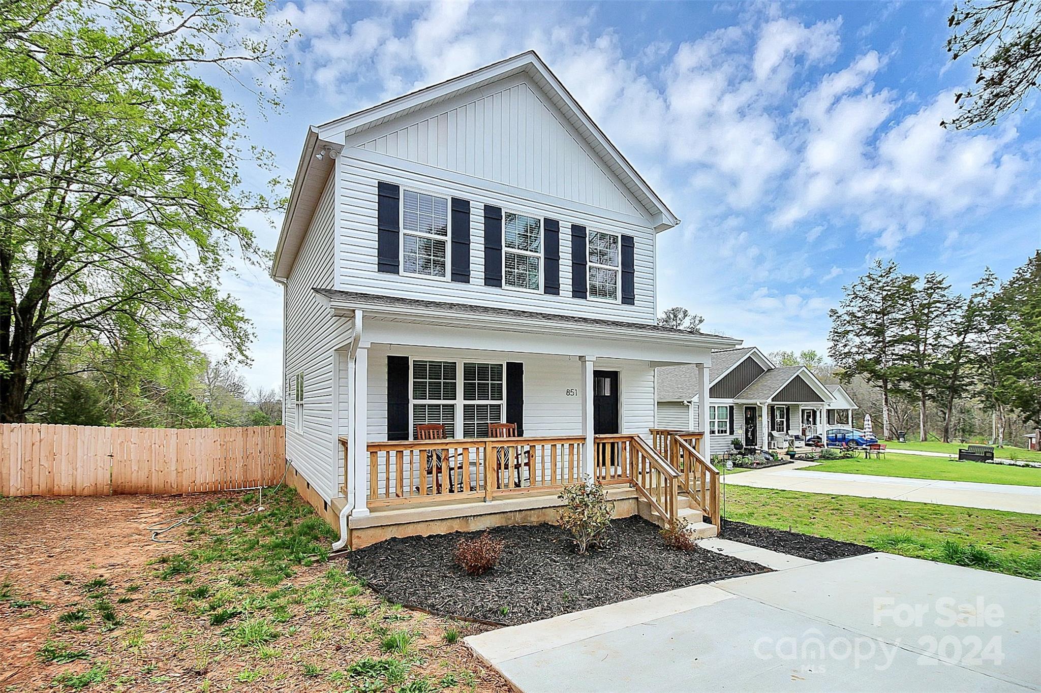 White two-story house with black shutters, a covered porch, and a wooden privacy fence.