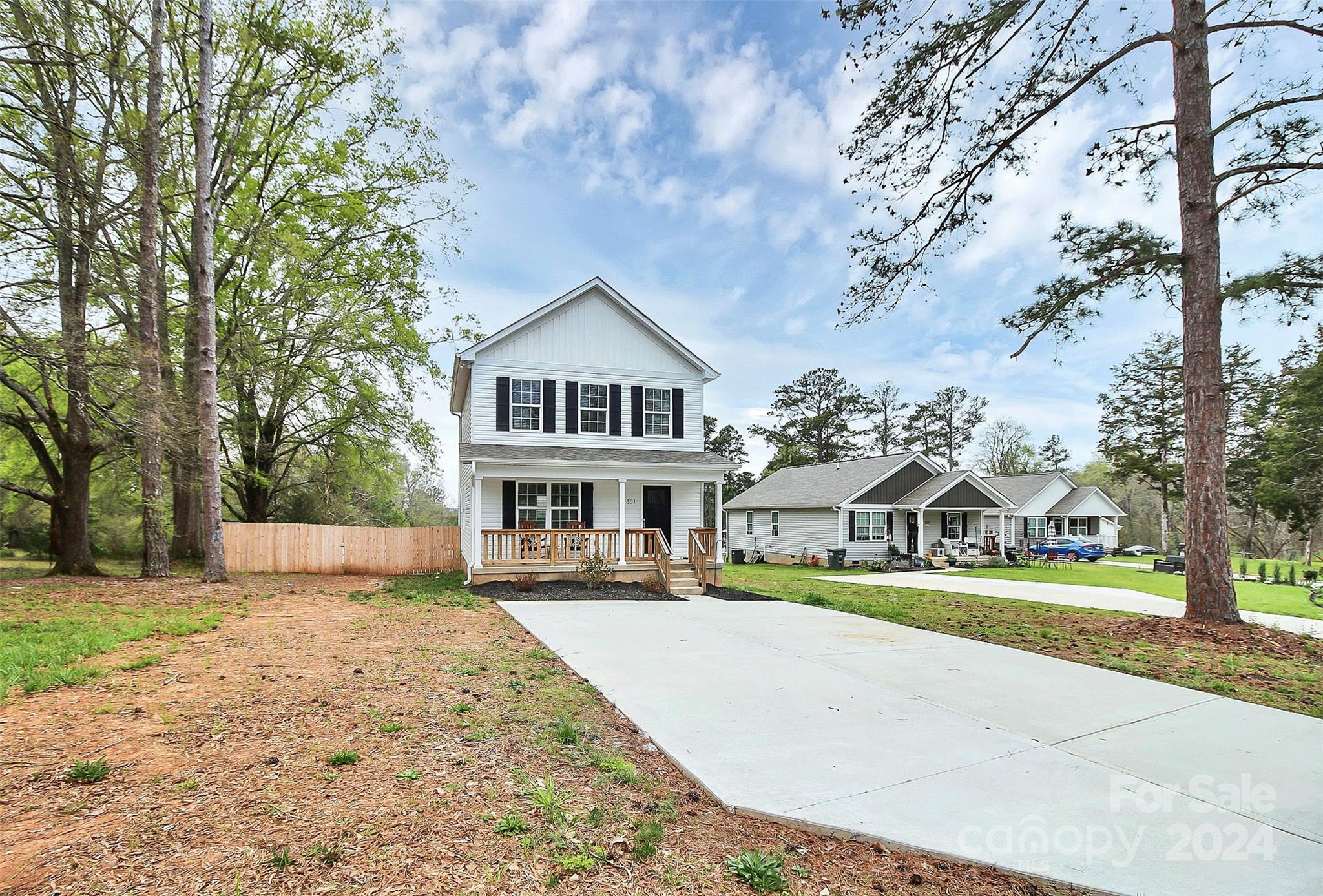 White two-story house with black shutters, a covered porch, and a broad concrete driveway.