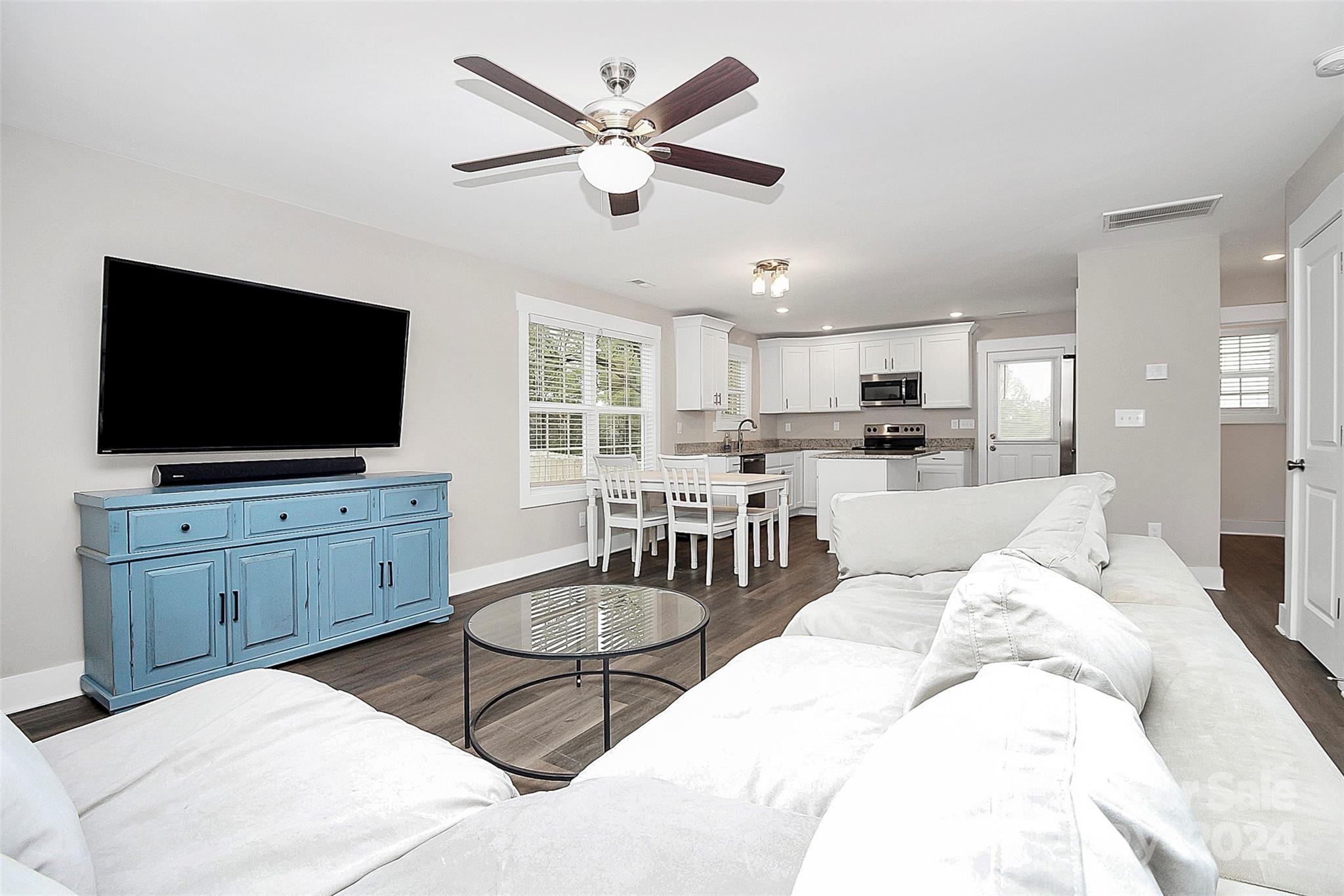 Open-plan living room with a white sectional, blue media cabinet, and adjoining white kitchen.