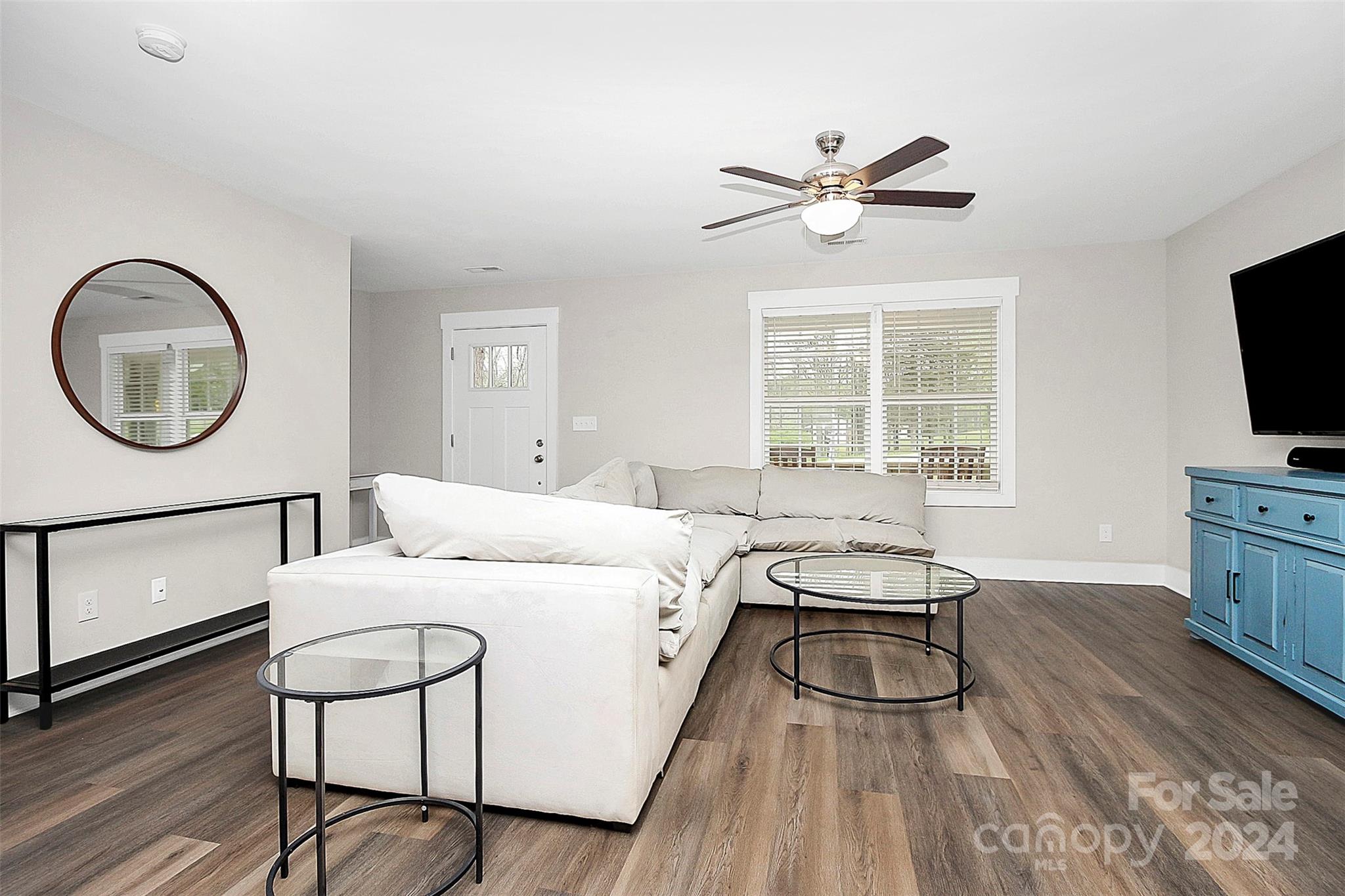 Living room with a white sectional, glass coffee tables, dark flooring, and a blue media cabinet.