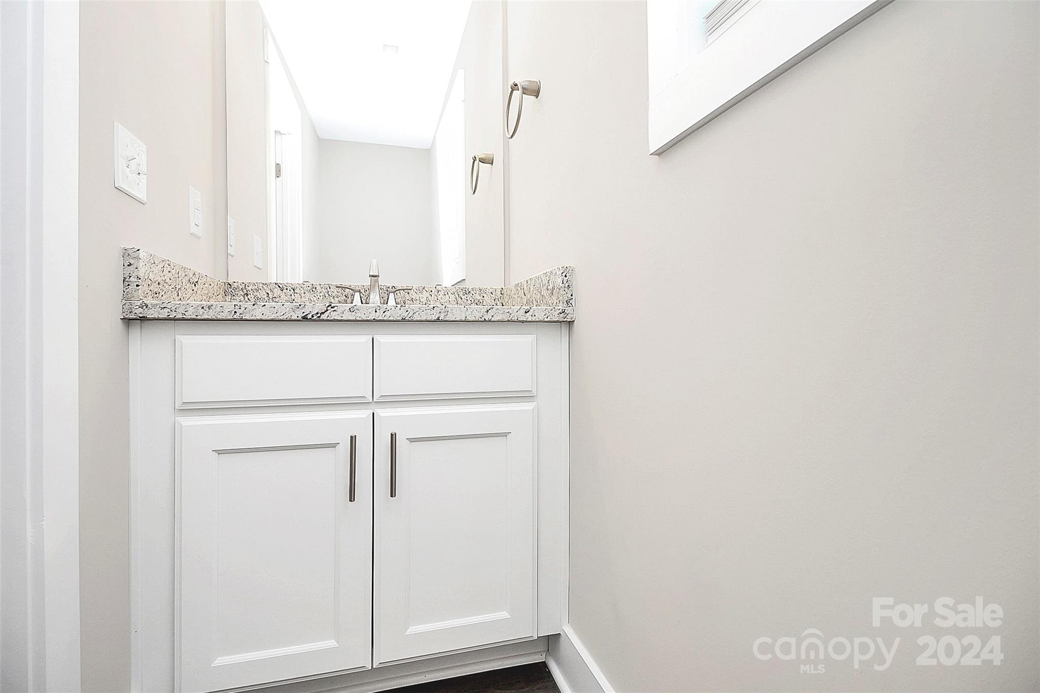 Bathroom vanity with white cabinets, speckled stone countertop, undermount sink, and large mirror.