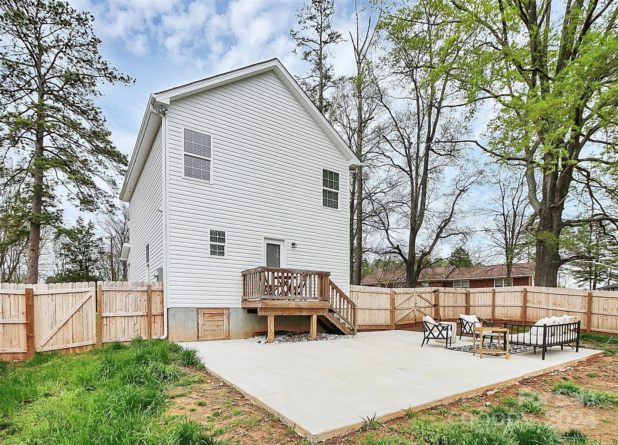 Rear of a white two-story house with a wooden deck, fenced yard, and concrete patio seating.