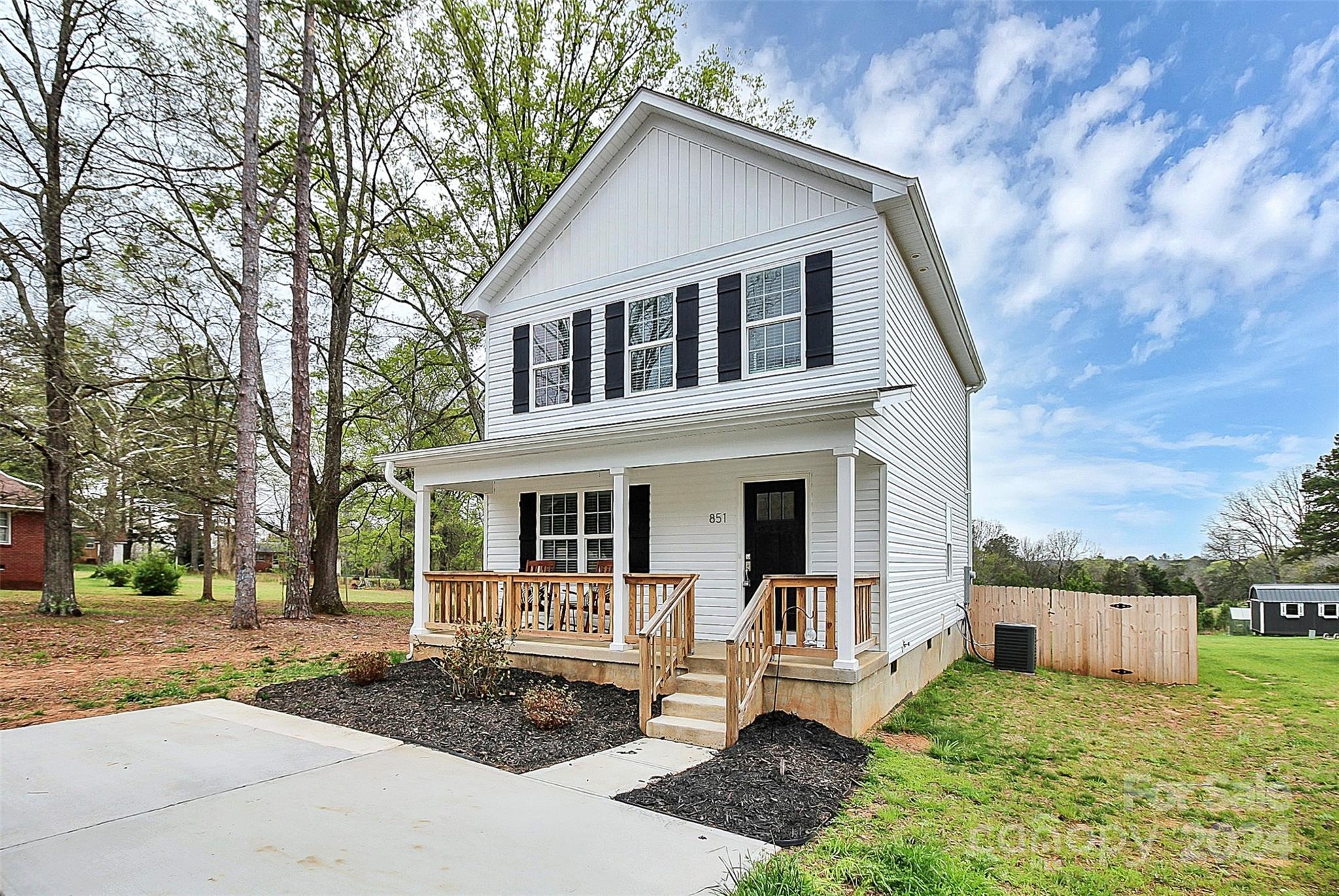 Two-story white house with a covered wood-railed porch, black shutters, and a concrete driveway.