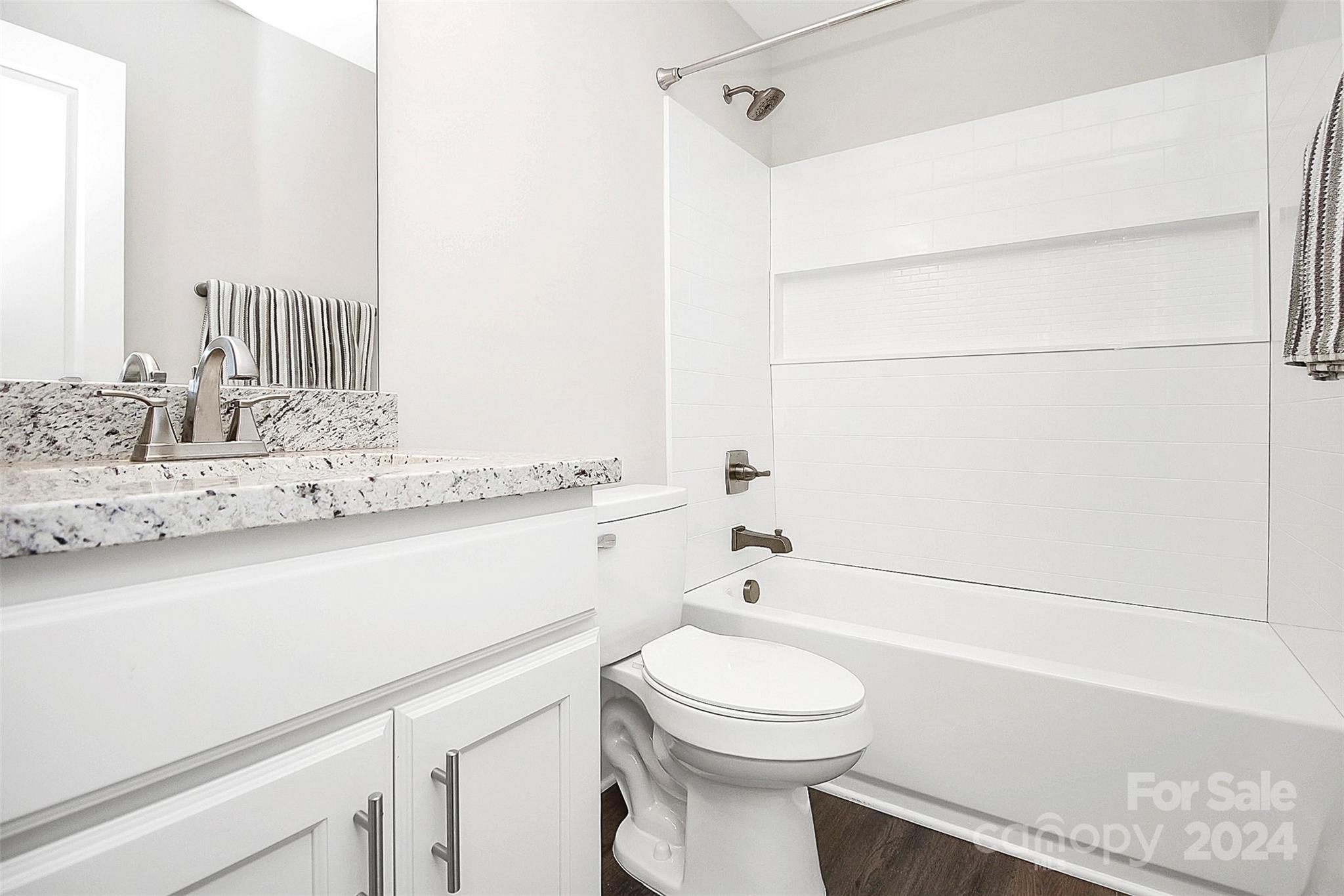 Bathroom with a granite vanity and white tiled tub and shower with a recessed shelf.