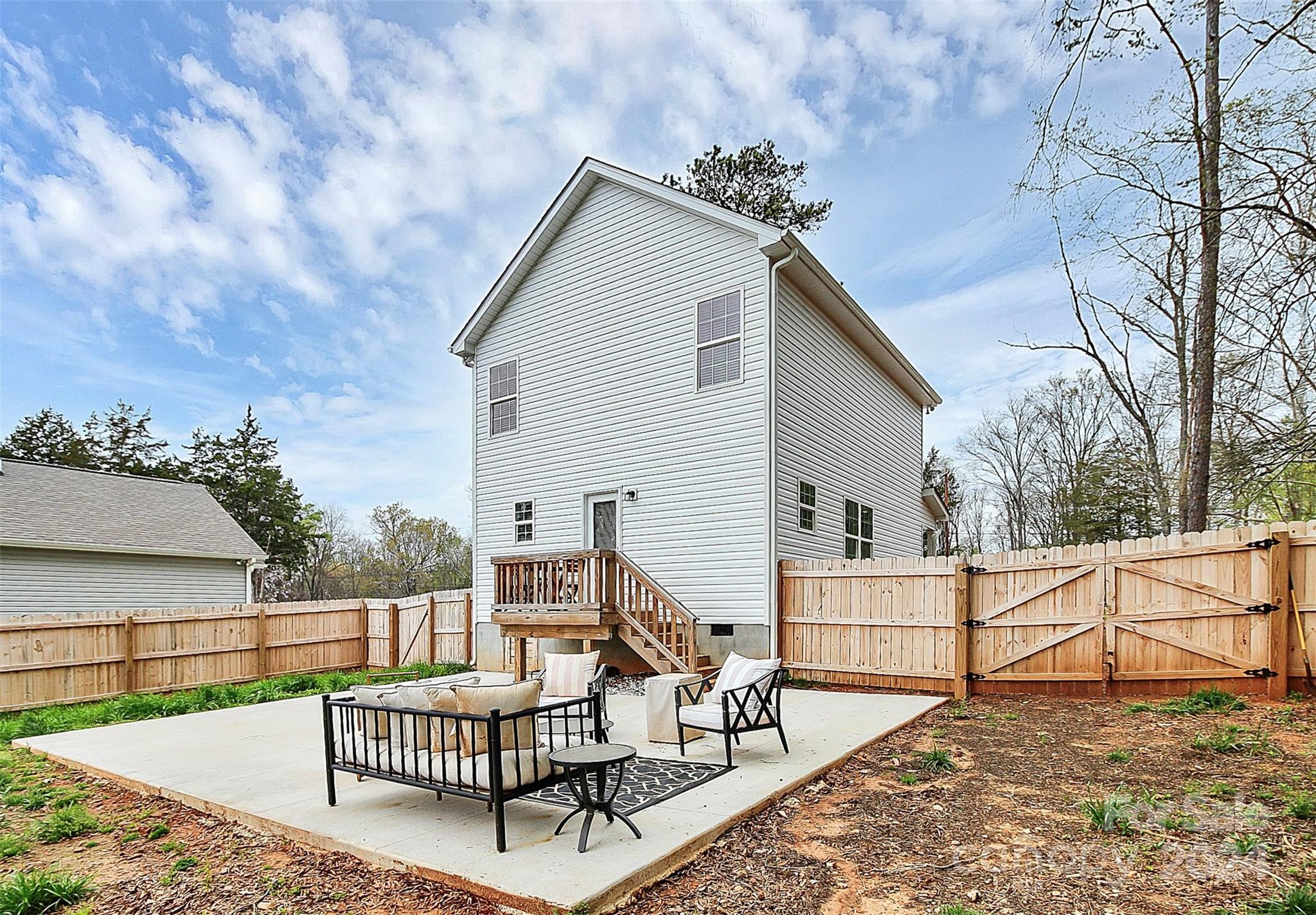 White two-story home's fenced backyard with a raised deck and furnished concrete patio.