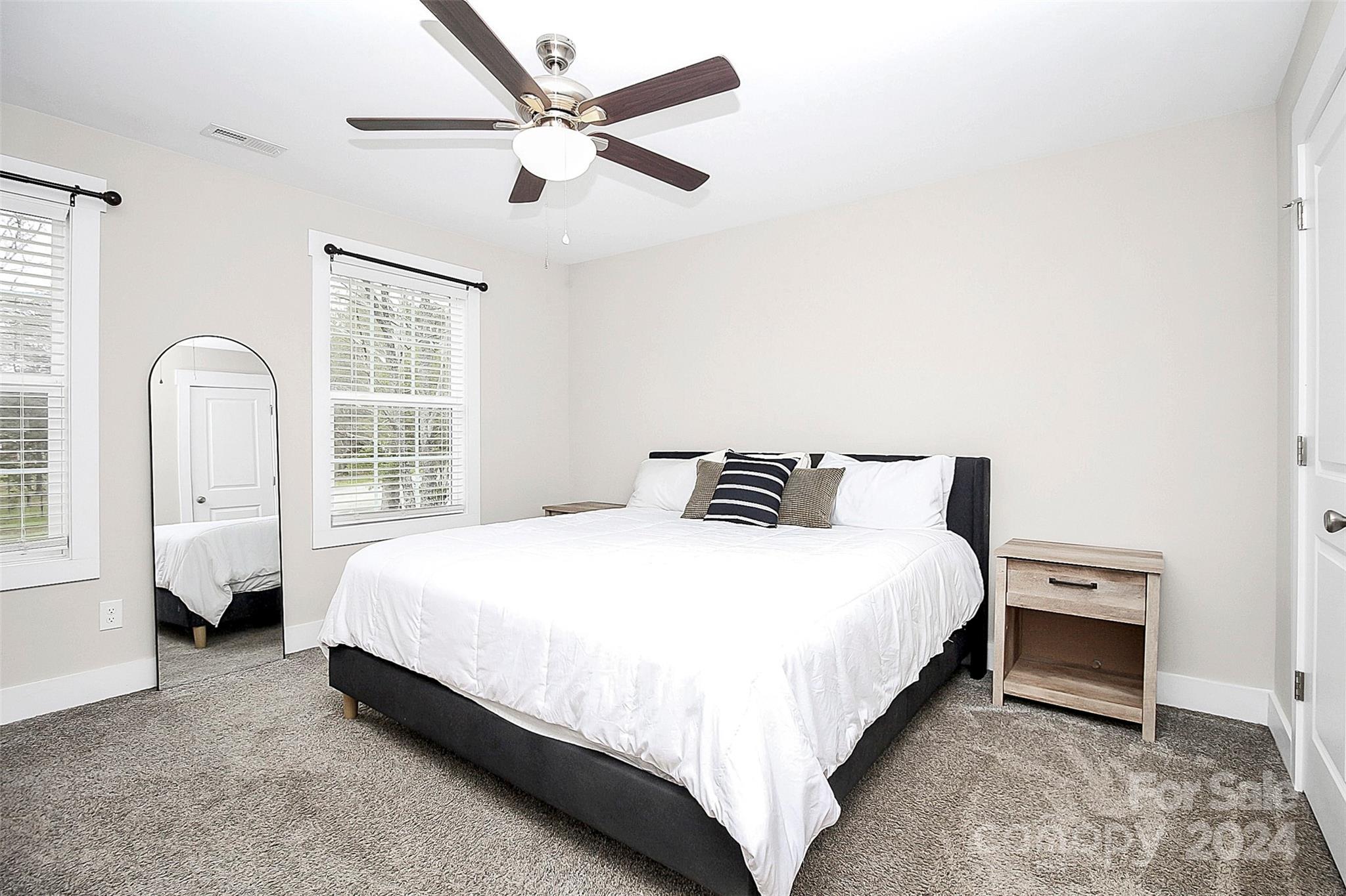 Bedroom with a white bed, dark accent pillows, gray carpet, and ceiling fan.