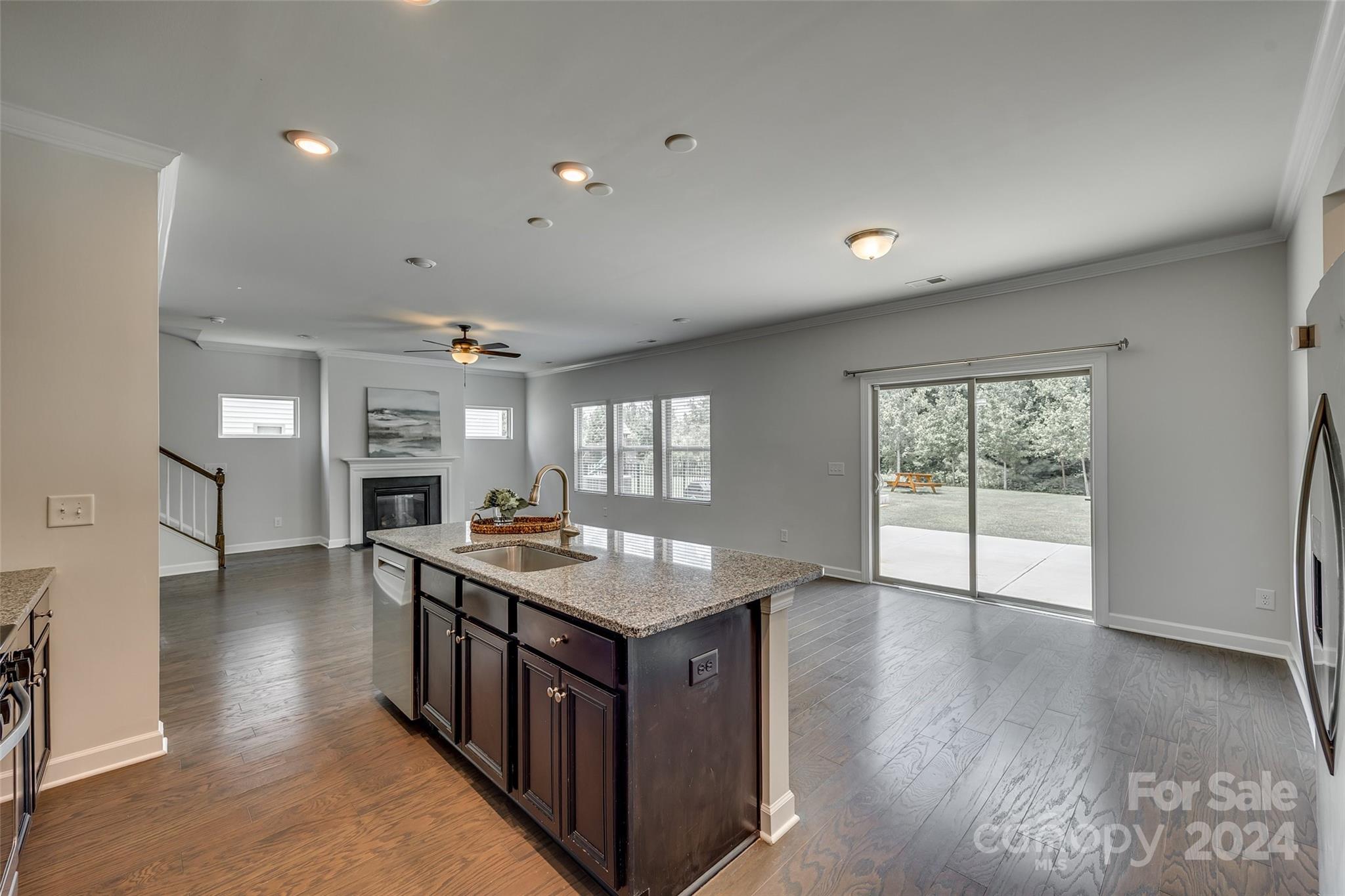 Open kitchen with a granite island overlooks a living area with a fireplace and backyard patio.