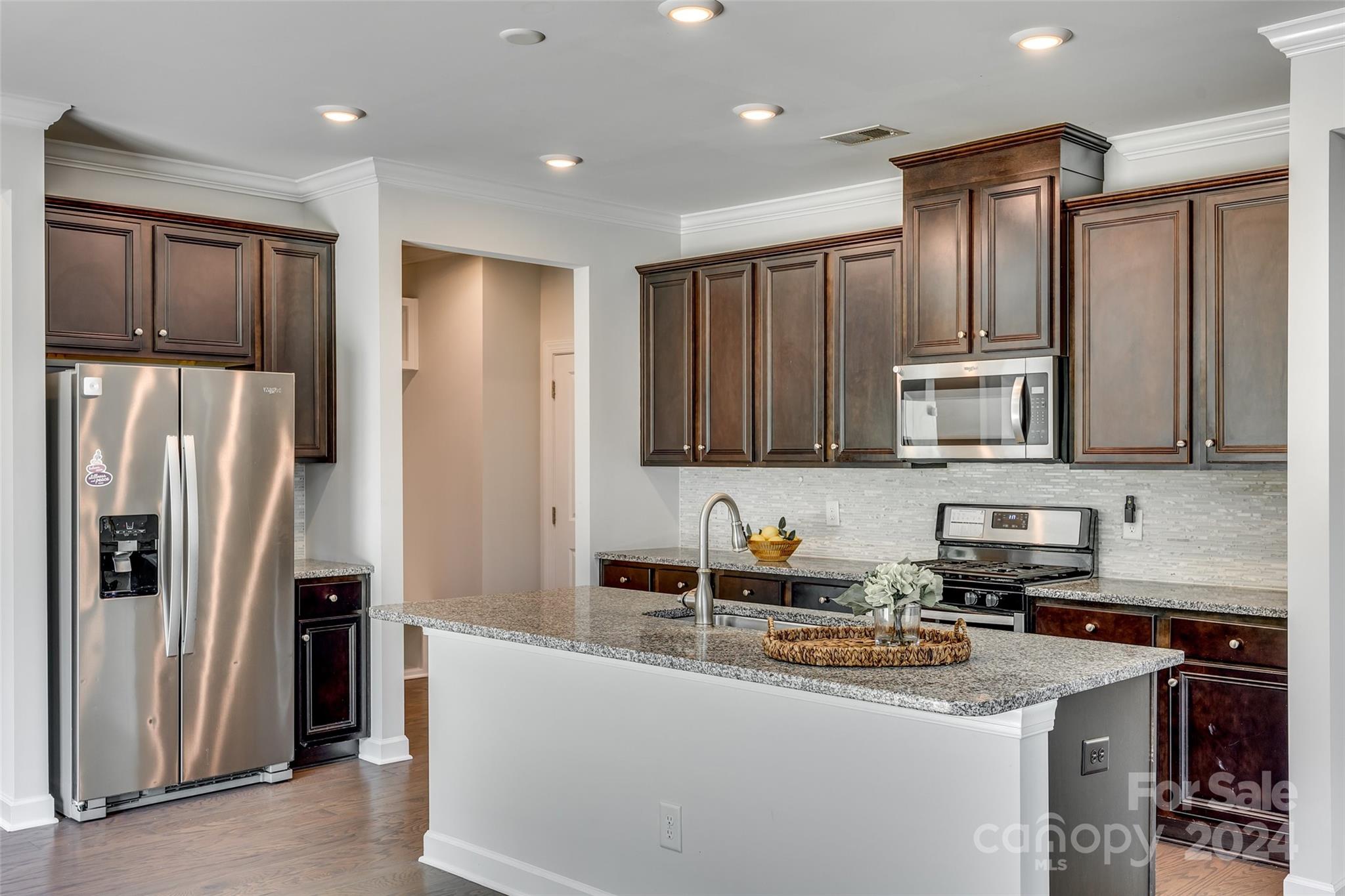 Kitchen with dark wood cabinets, stainless steel appliances, and a granite island with a sink.