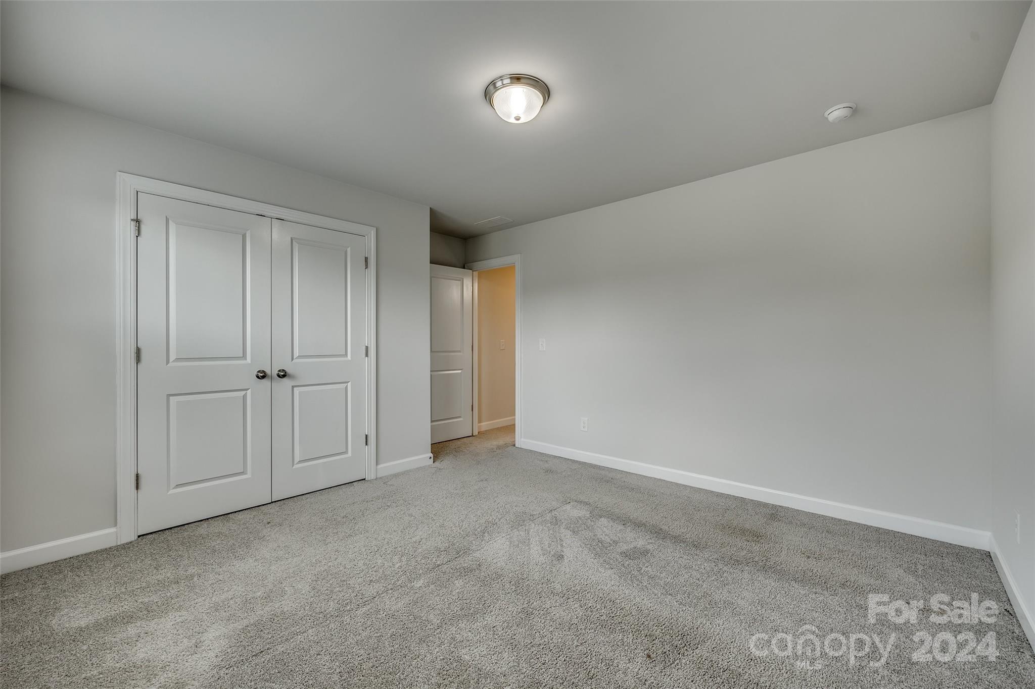 Empty carpeted room with double closet doors and an open doorway to a warmly lit hall.