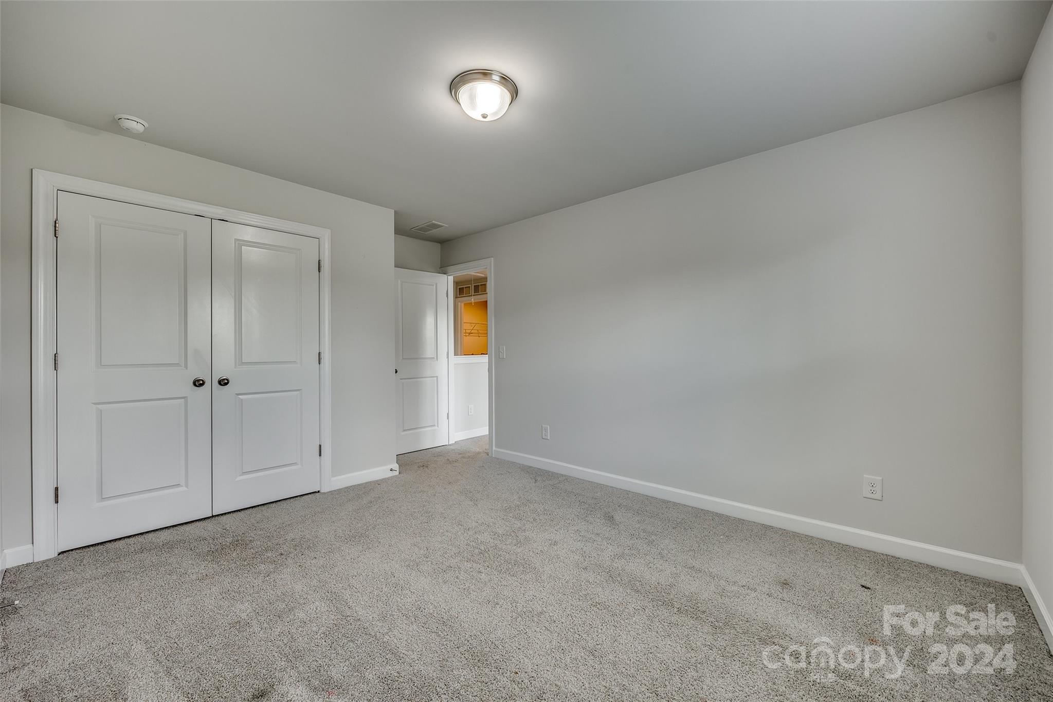 Empty bedroom with gray carpet, white double closet doors, and an open doorway to a lit closet.