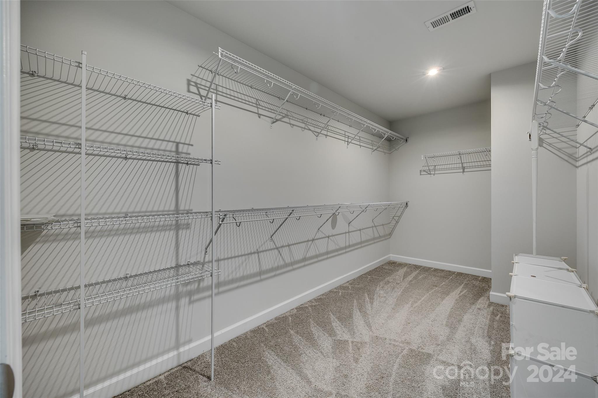 Walk-in closet with extensive wire shelving, carpeted floor, and white drawer units.