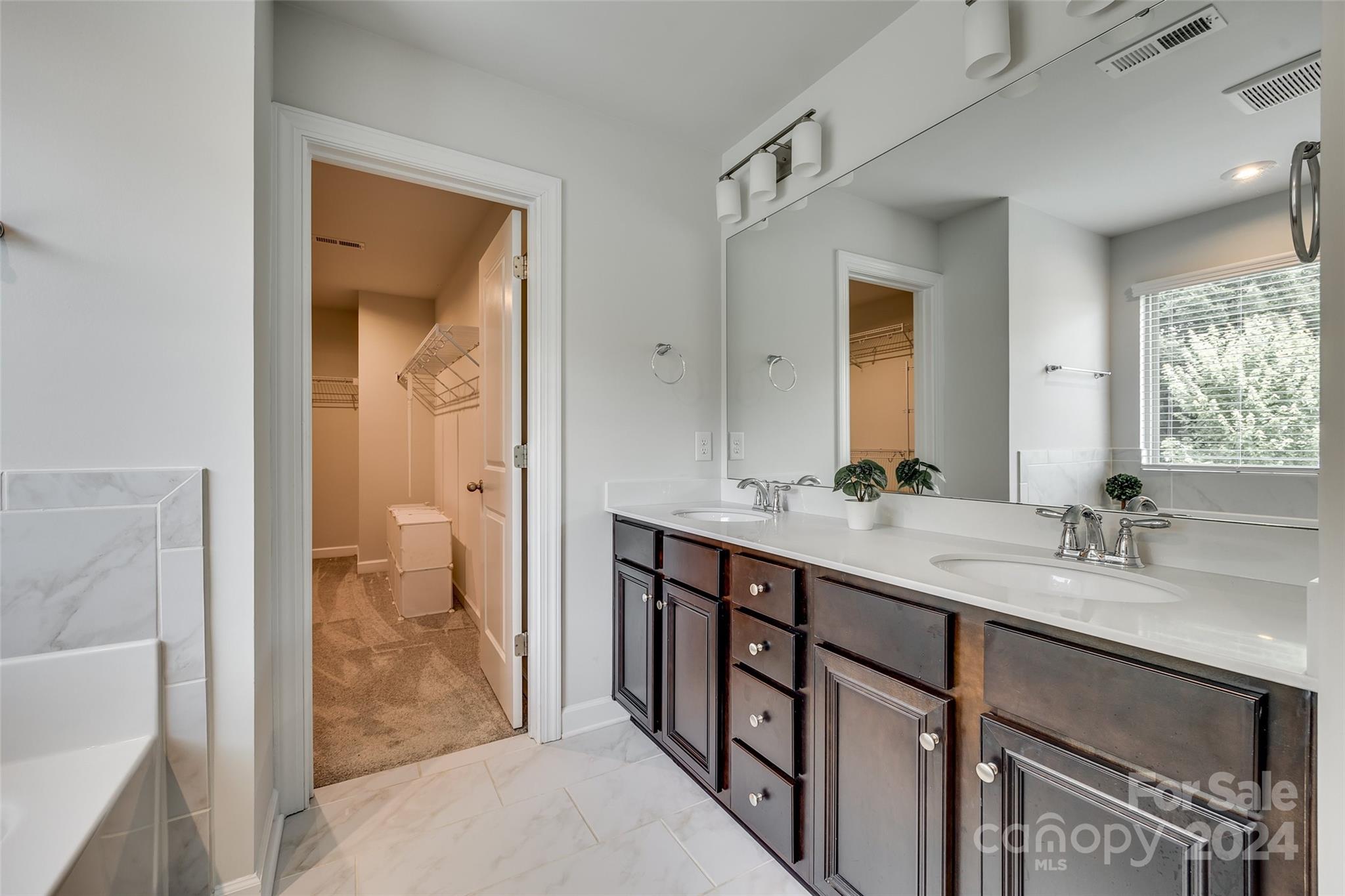 Bathroom with a dark-wood double vanity and an open doorway to a walk-in closet.