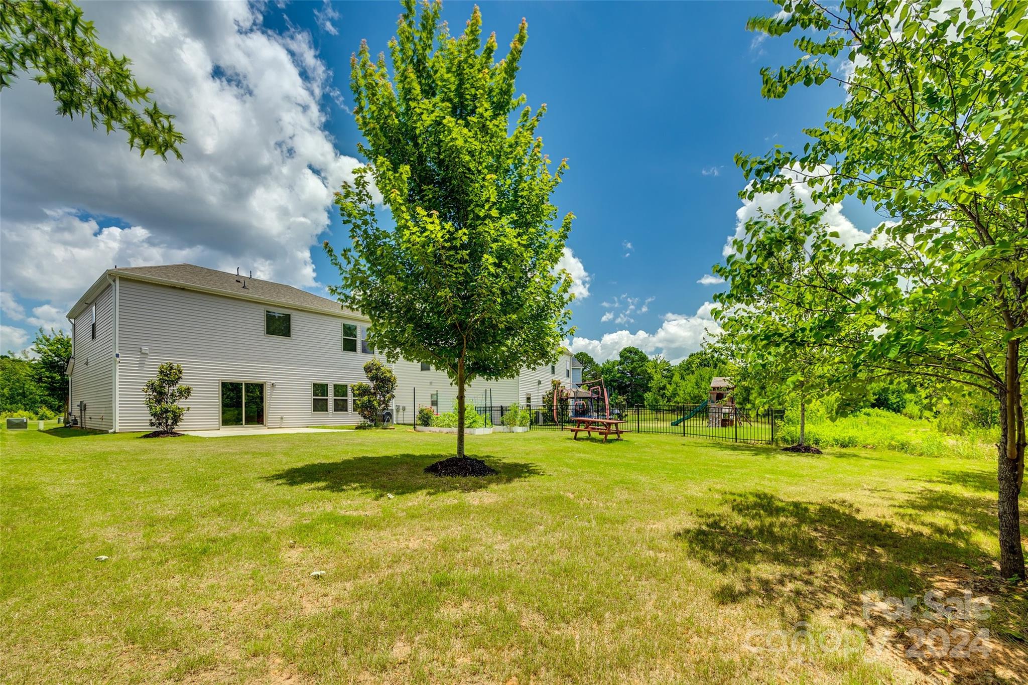 Two-story home behind a broad lawn, with mature trees and a fenced playground.