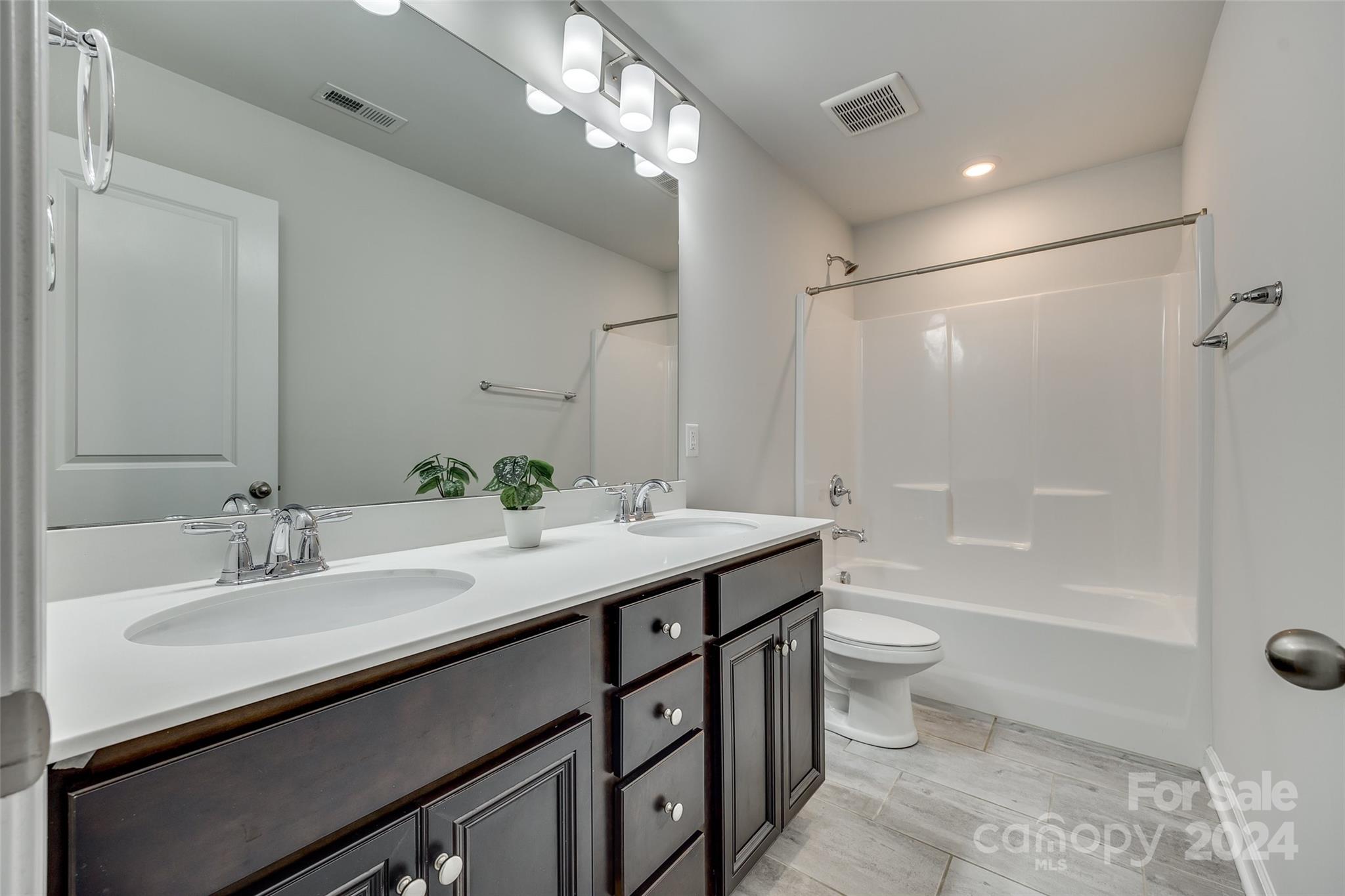 Bathroom with a dark double vanity, large mirror, and white tub-shower surround.