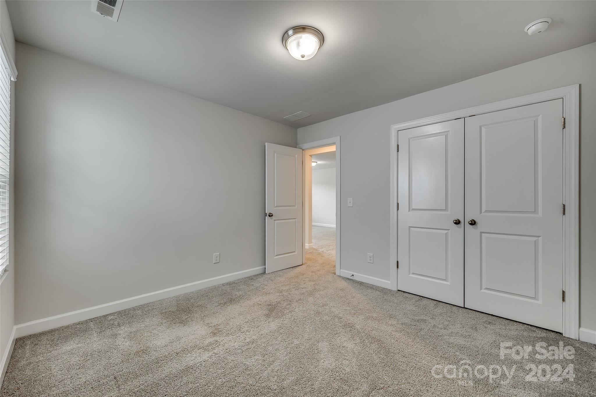 Empty bedroom with beige carpet, white double closet doors, and an open doorway.