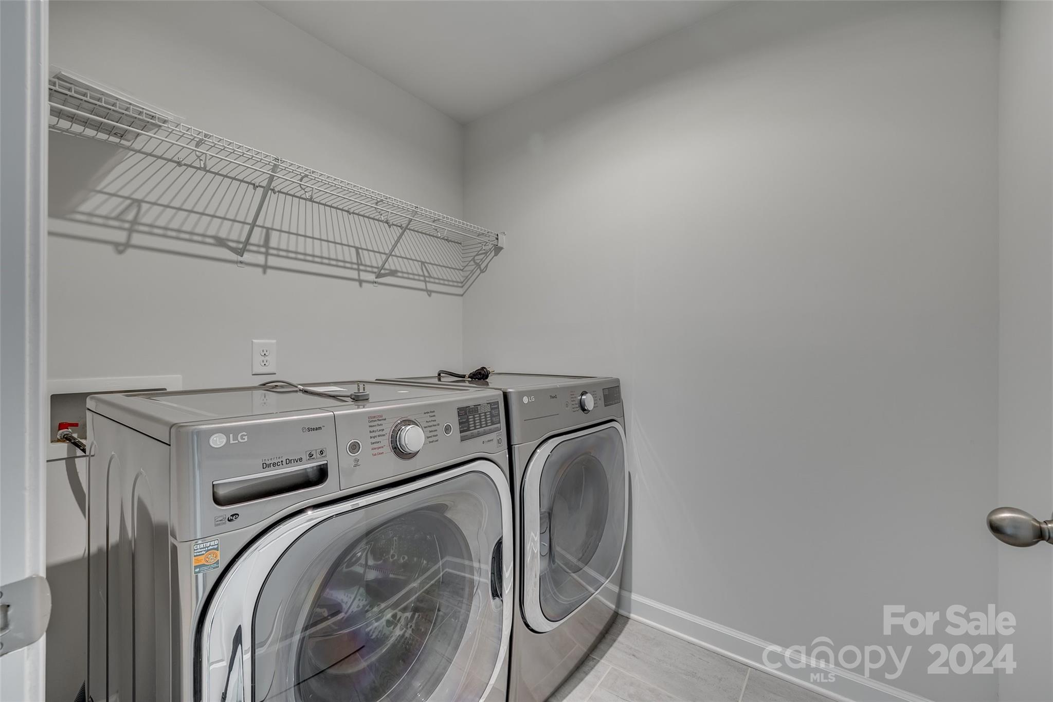 Laundry room with front-loading washer and dryer beneath a long wire shelf.