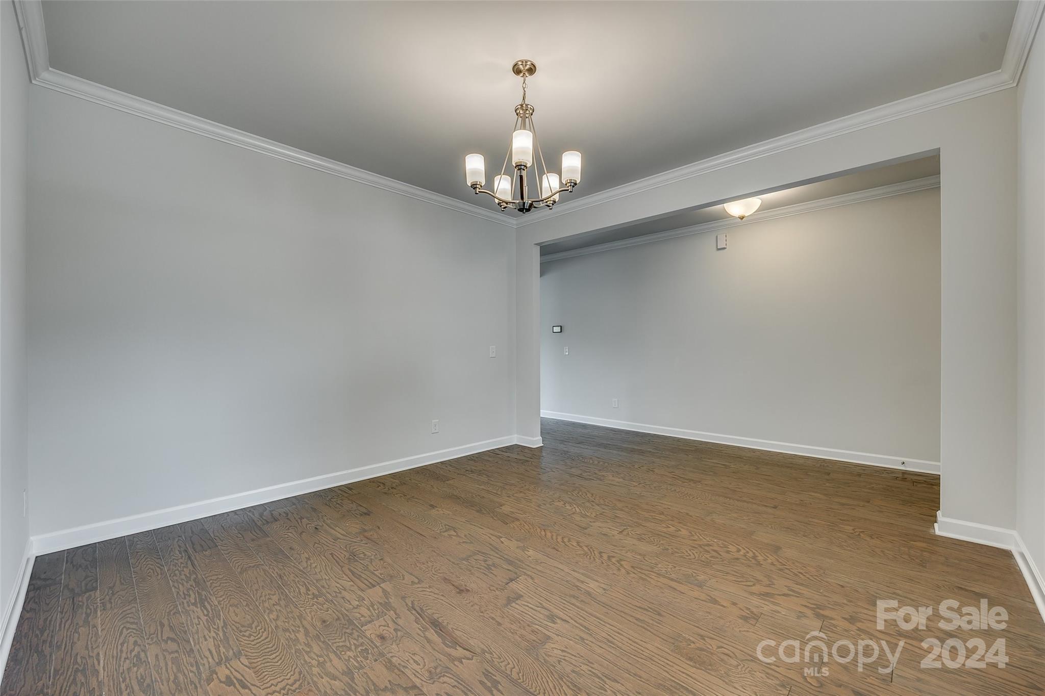 Vacant dining room with hardwood floors, crown molding, and a brass chandelier.