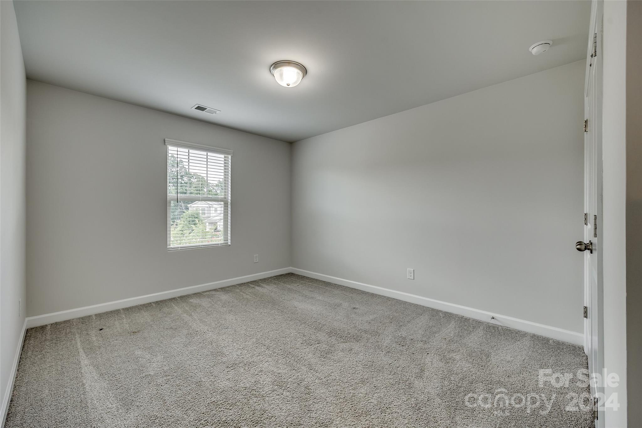 Empty bedroom with gray carpet, white walls, and a window with blinds.