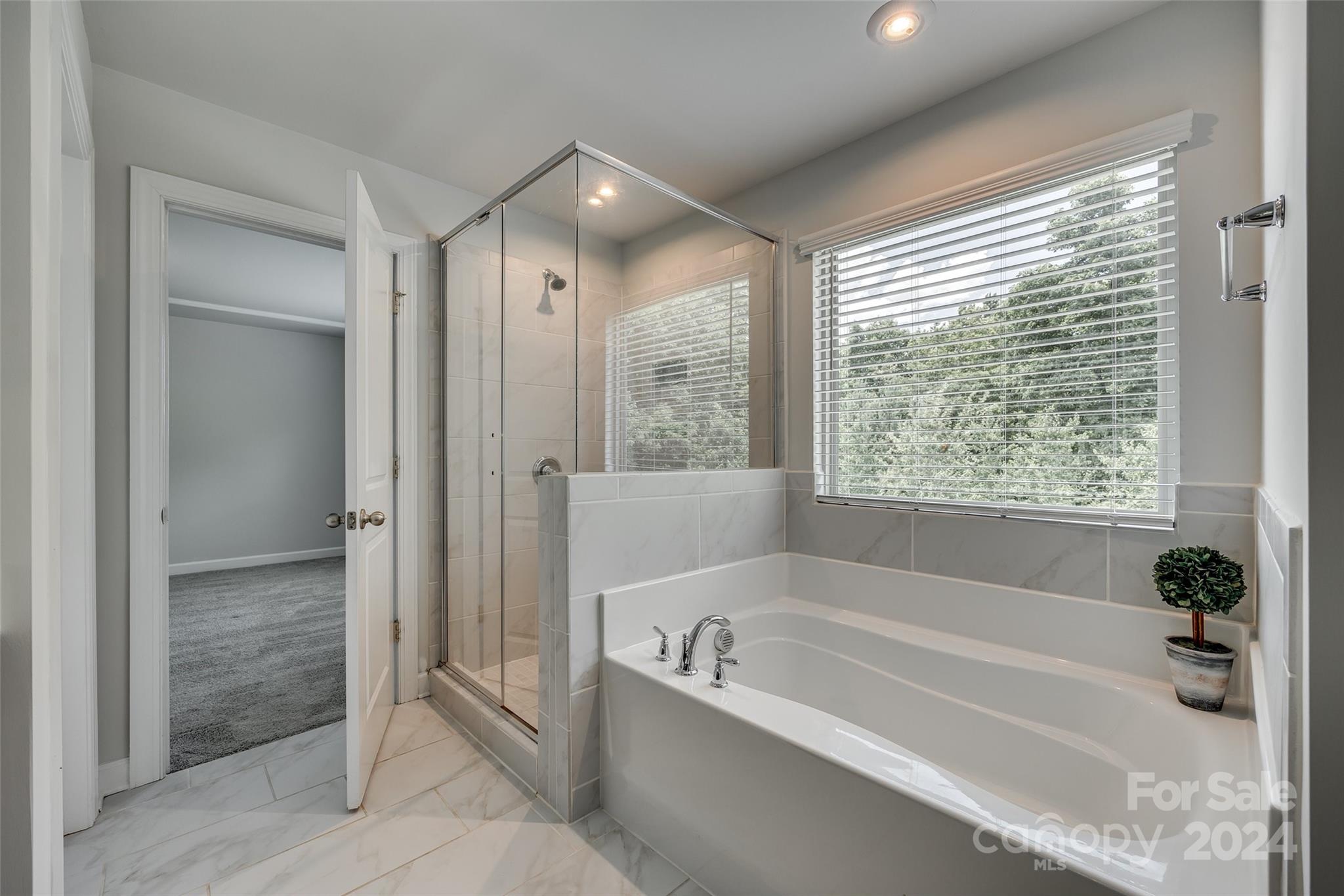 Bathroom with a soaking tub, glass shower, and wide window overlooking trees.