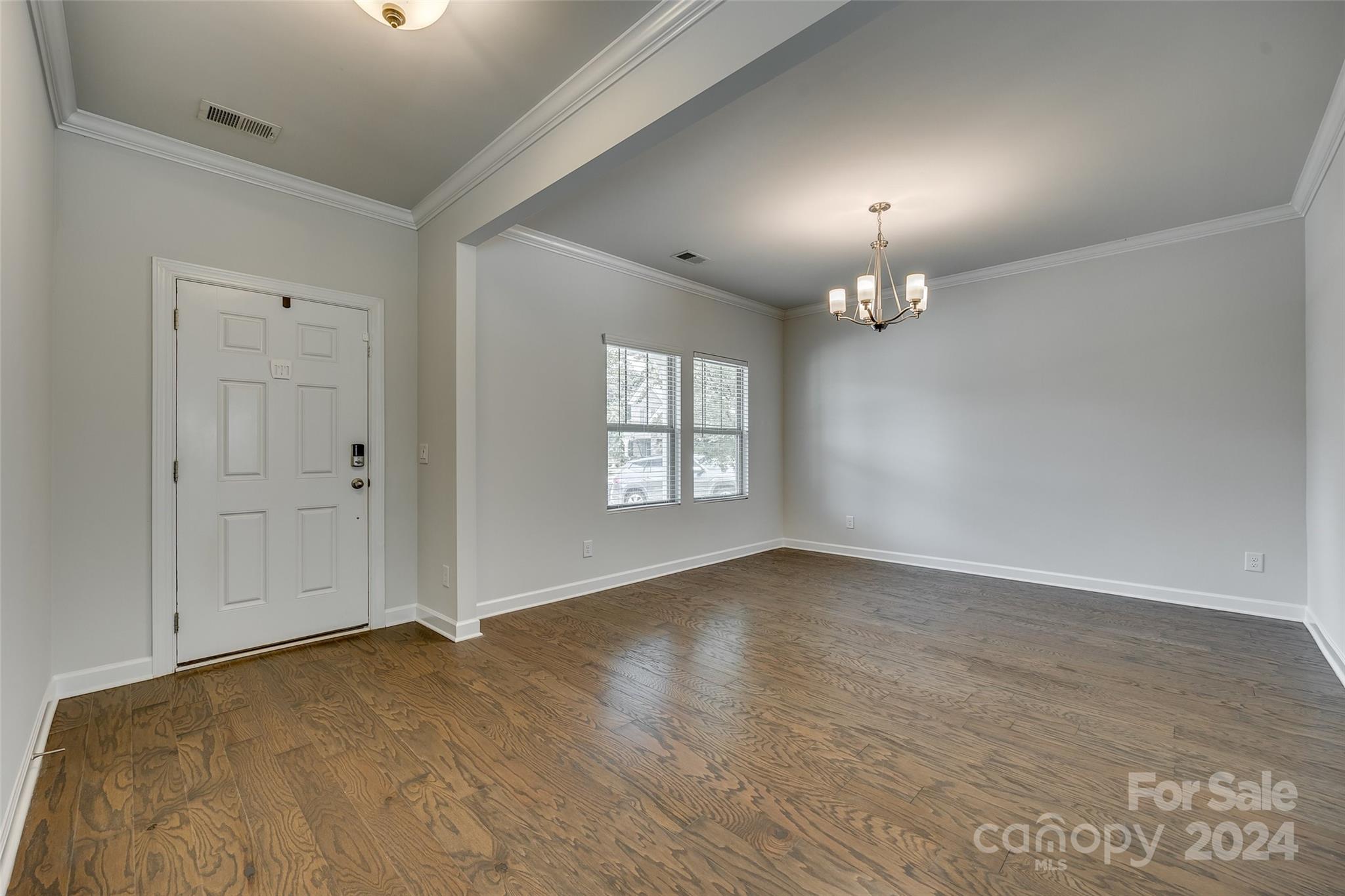 Empty dining area with wood floors, a chandelier, and windows beside the entry door.