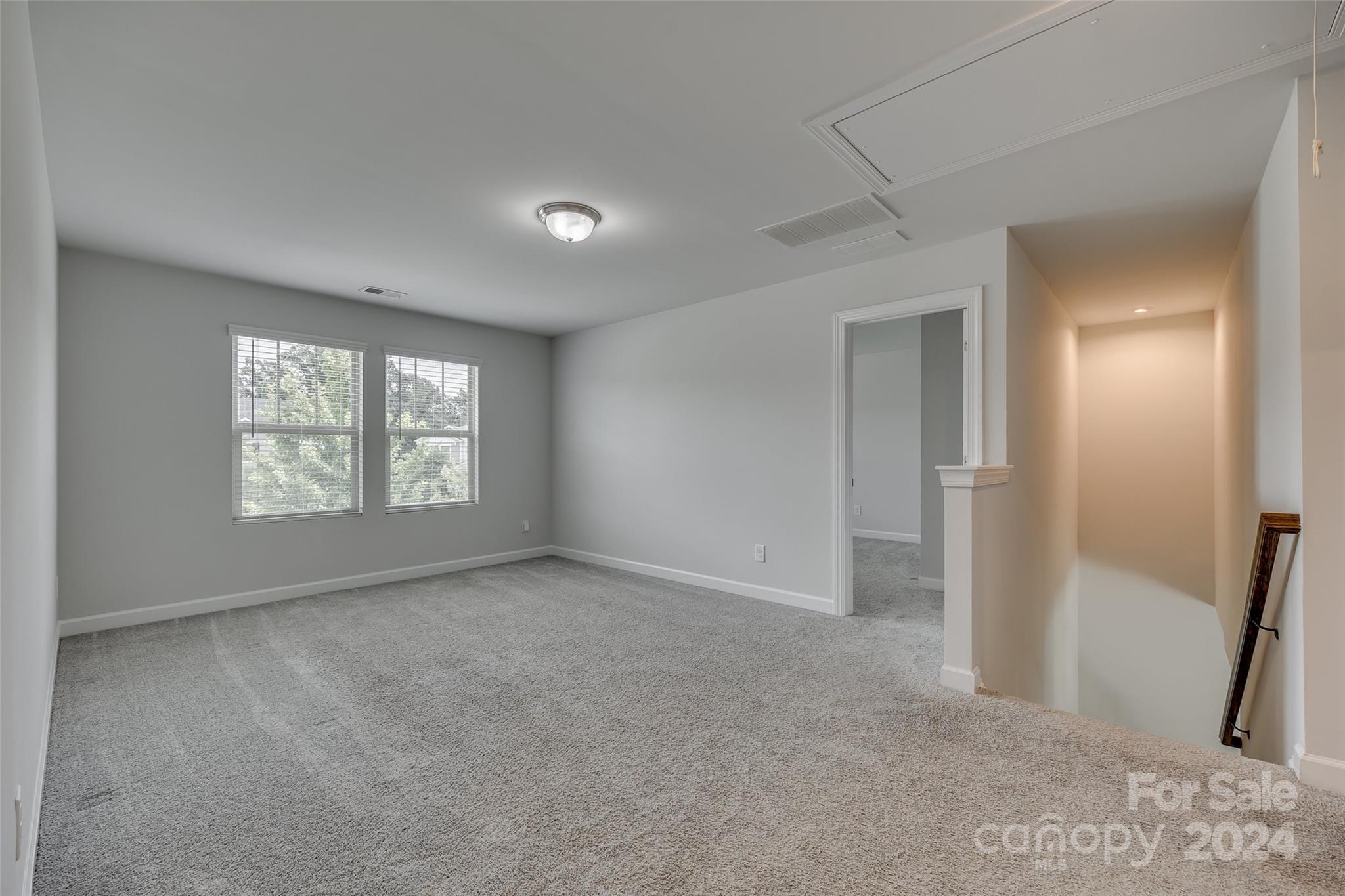 Empty carpeted upstairs room with two windows and an open doorway beside the staircase.
