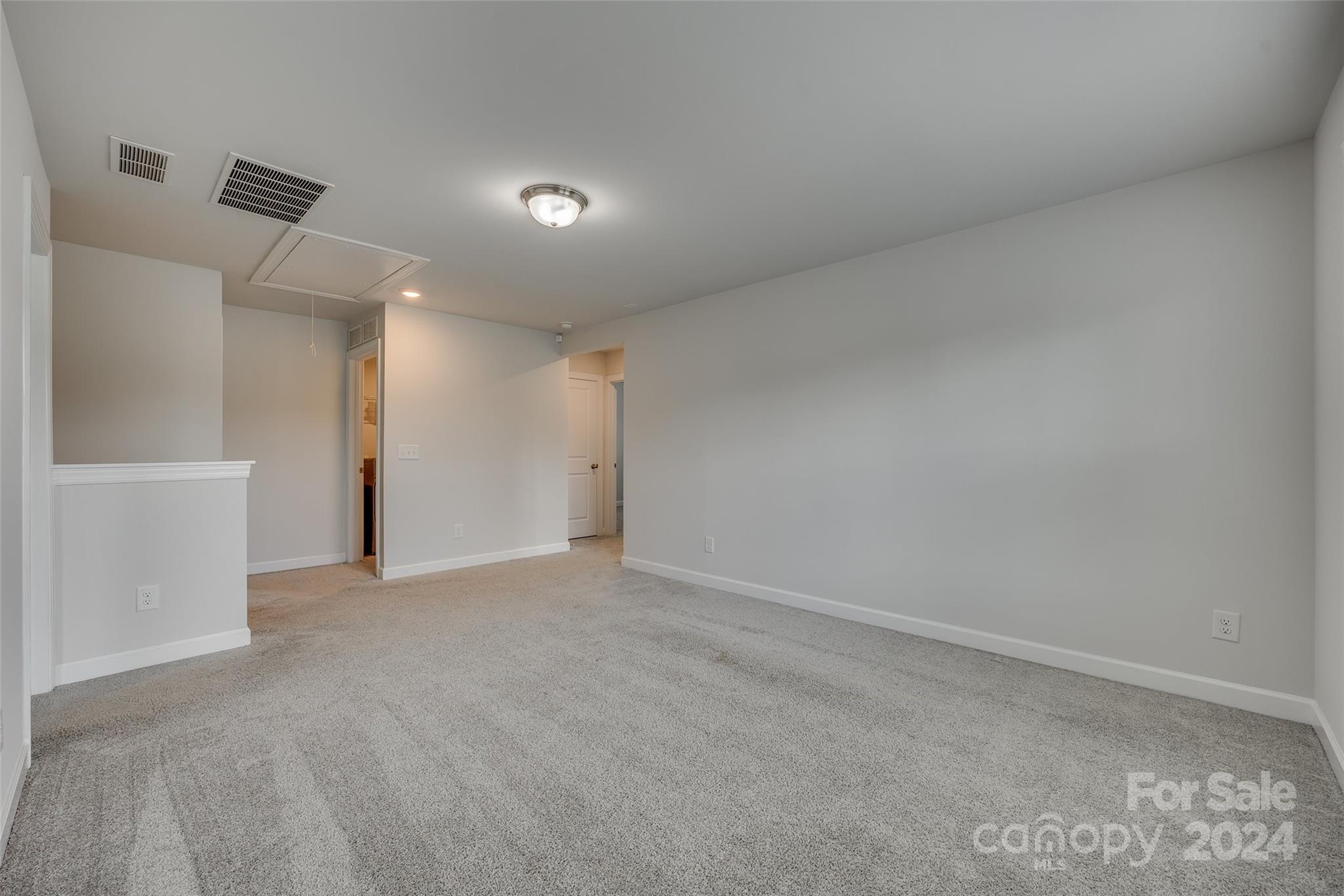 Empty carpeted room with gray walls, a half-height partition, and ceiling vents.
