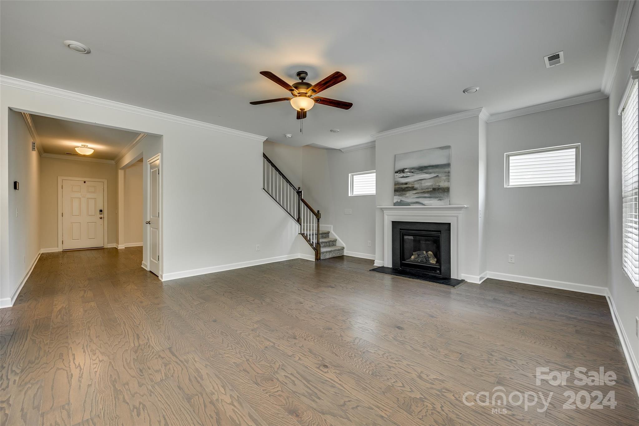 Empty living room with wood floors, a staircase, ceiling fan, and fireplace.