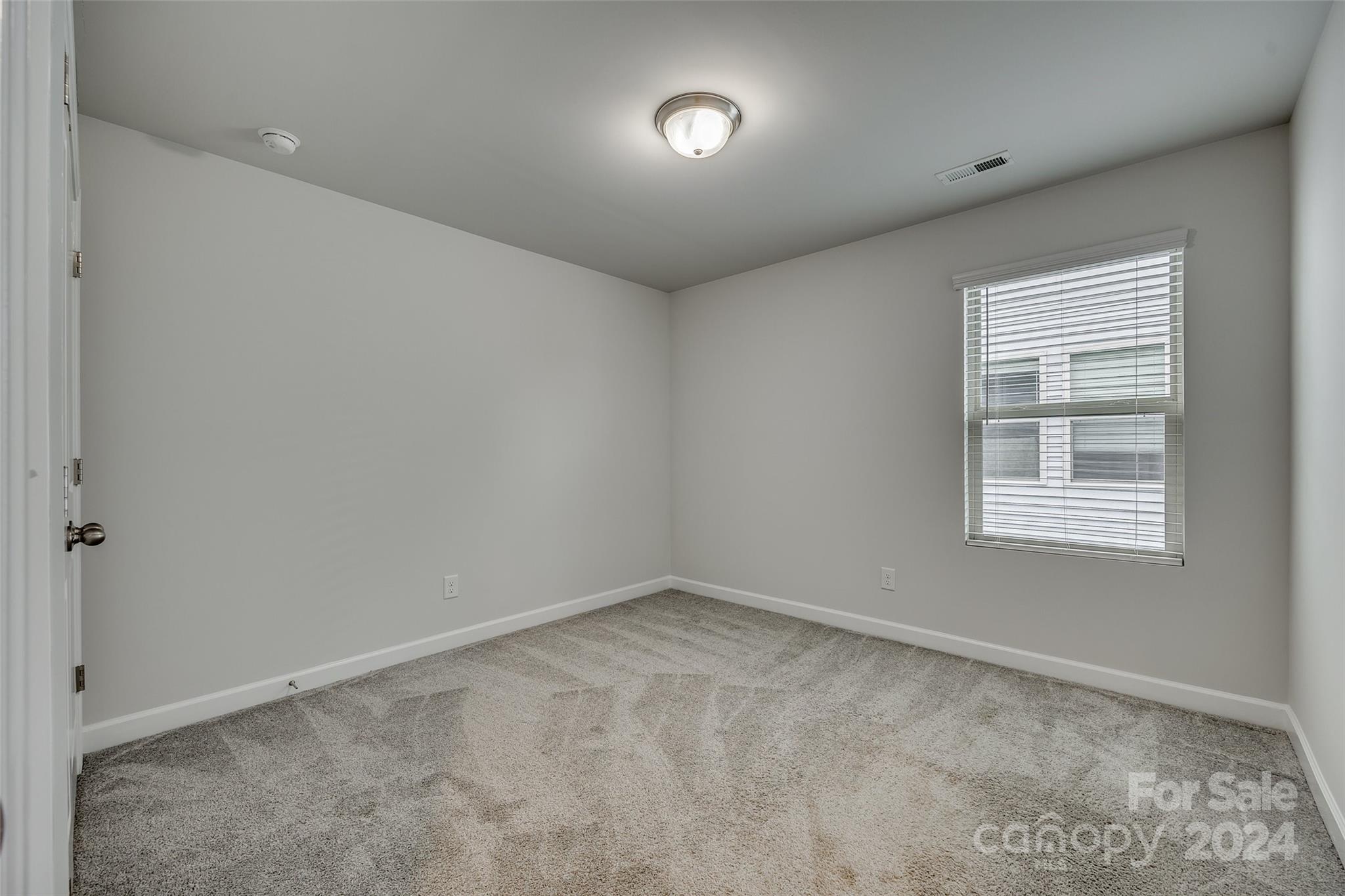 Empty carpeted room with gray walls and a window fitted with white blinds.