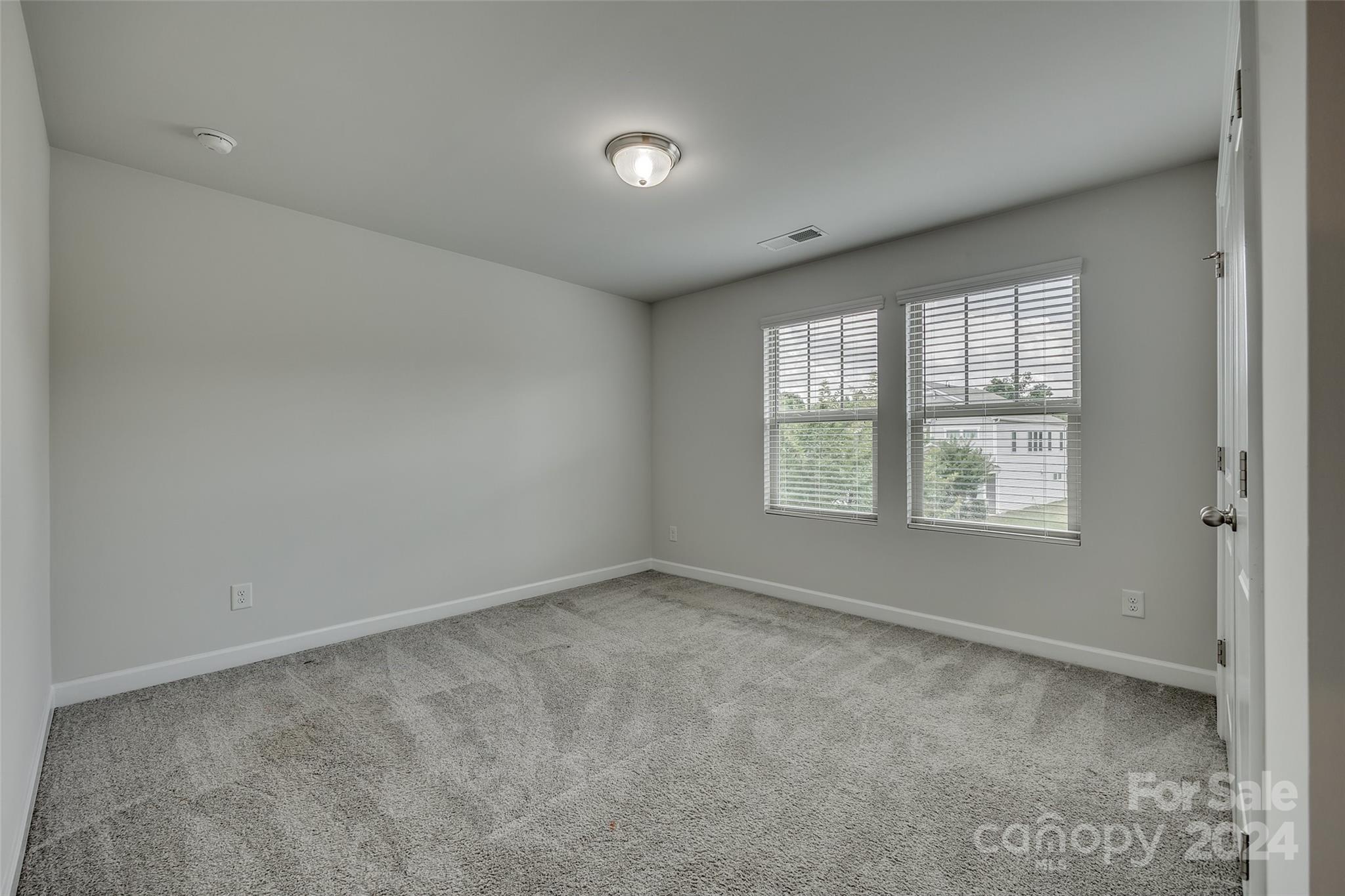 Empty bedroom with gray carpet and two windows fitted with blinds.
