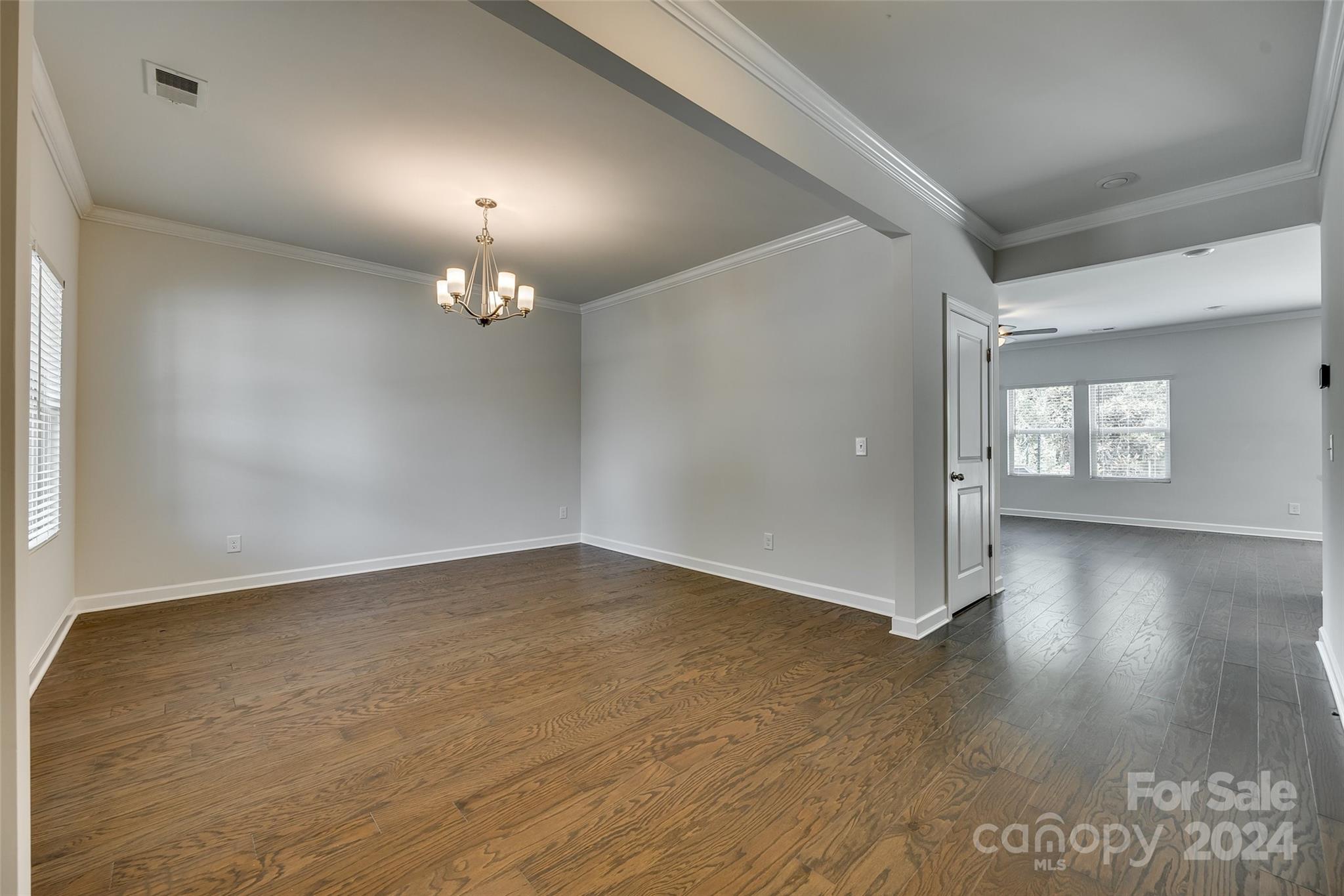 Empty dining room with wood floors, tray ceiling, and chandelier opening into a bright room with tile floors.