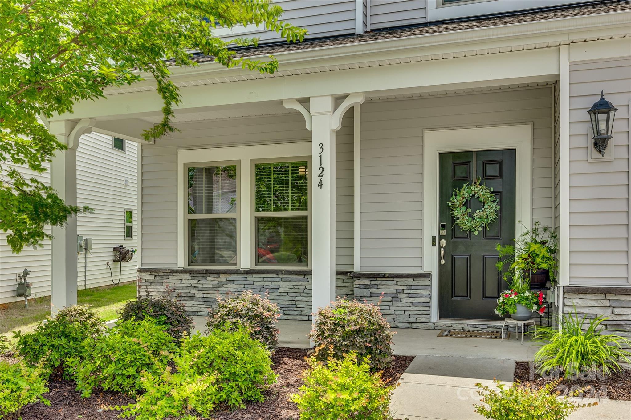 Front porch with a dark wreath-decorated door, stone veneer, and landscaped shrubs.