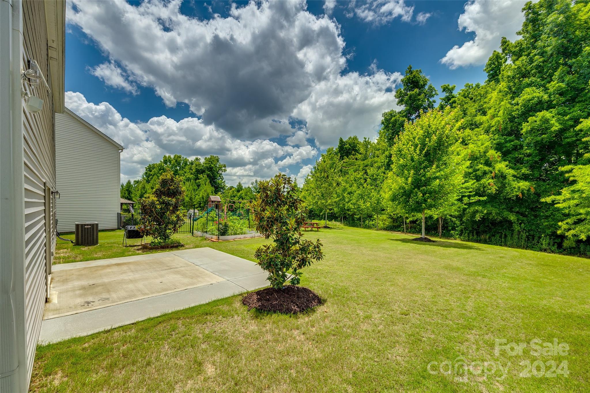 Backyard with a broad lawn, concrete patio, fenced garden, and playset beside the house.