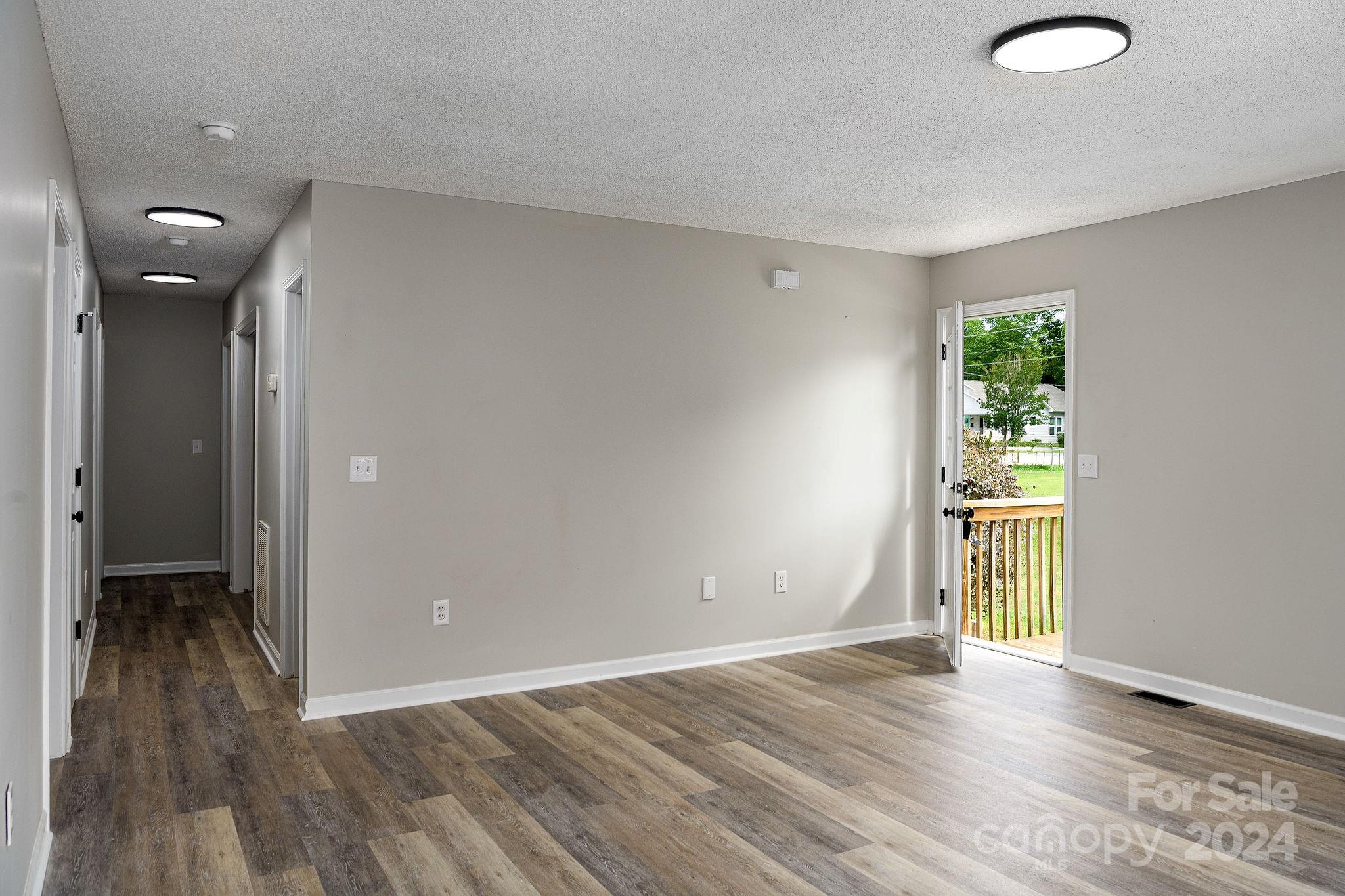 Empty room with wood-look flooring, a hallway, and an open door to a wooden deck.