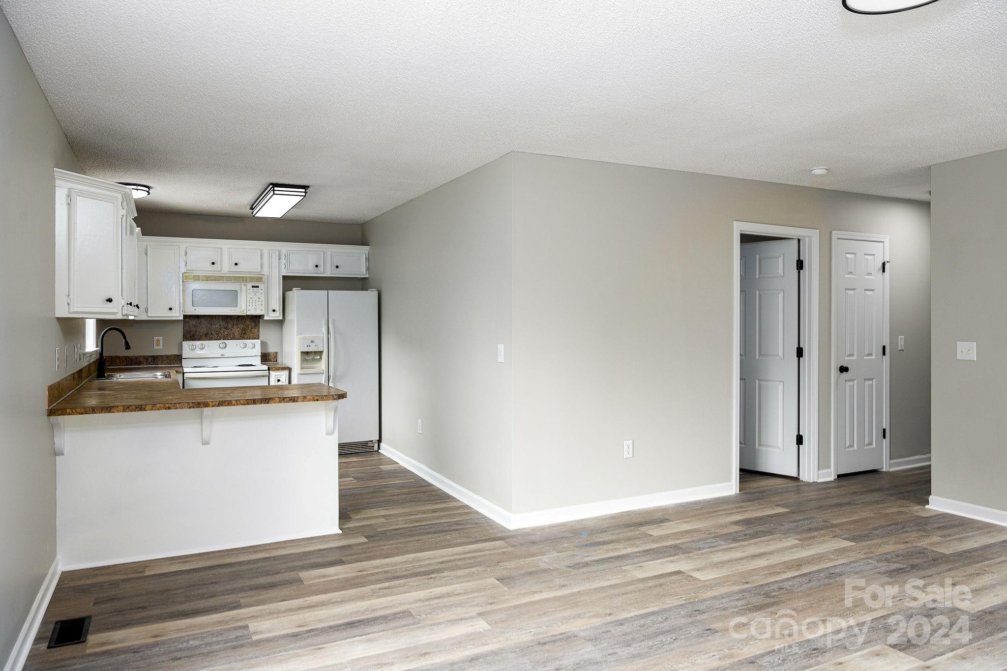 Open kitchen with white cabinets, brown breakfast bar, and wood-look flooring.