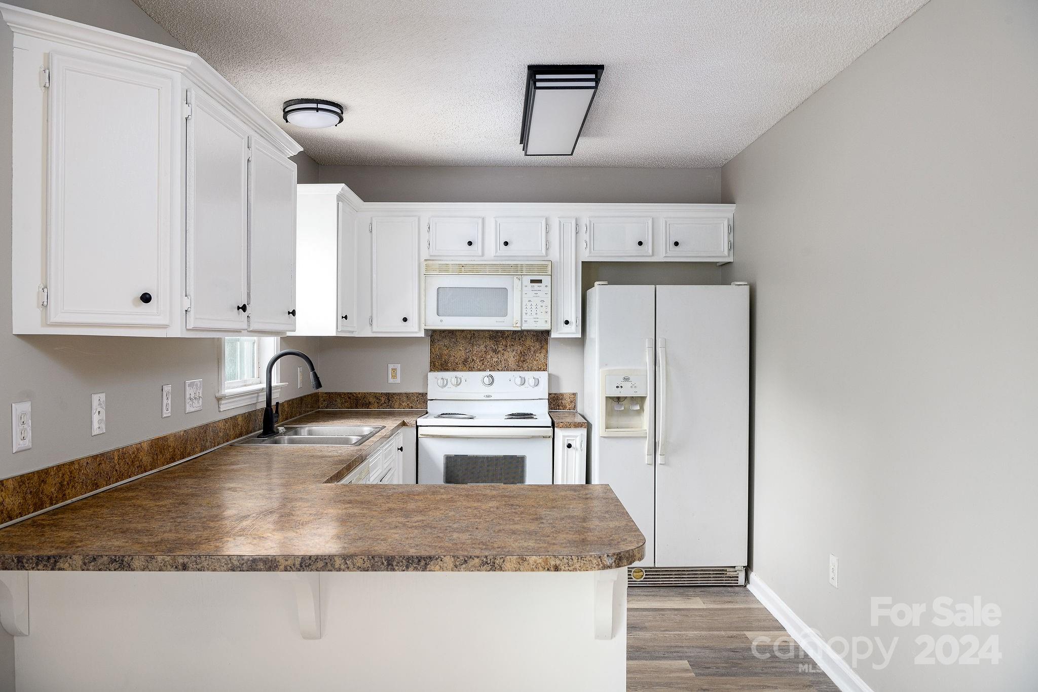 Kitchen with white cabinets, a brown-patterned peninsula, and white appliances.