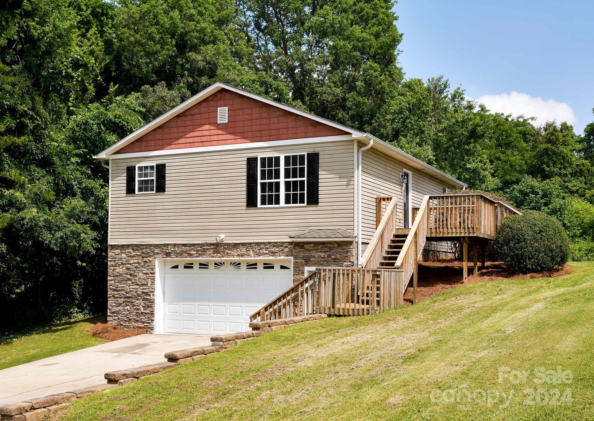 House with a stone-faced garage level and raised wooden deck on a sloping lawn.