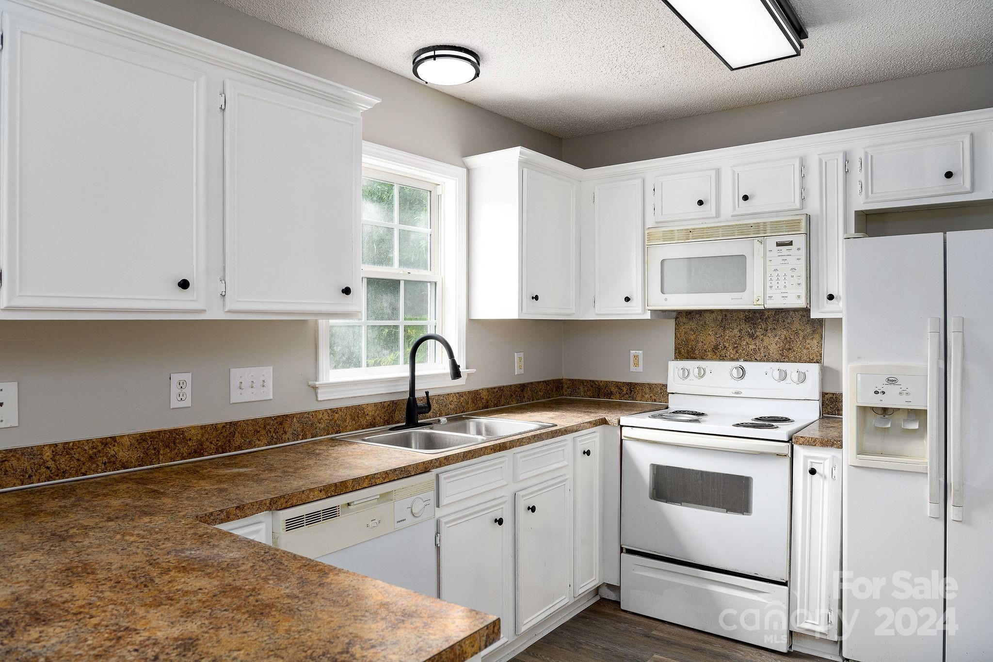 Kitchen with white cabinets, brown countertops, a double sink, and white appliances.