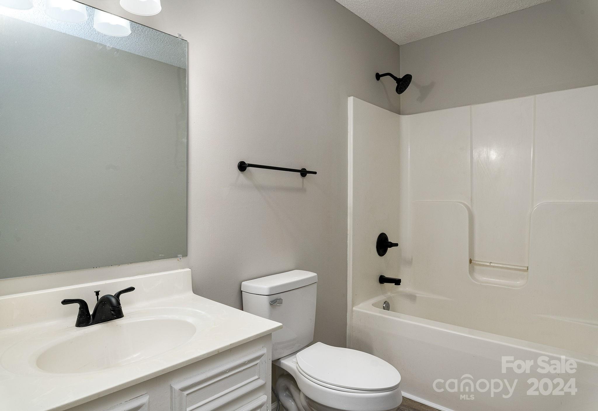 Bathroom with a white vanity, toilet, and tub-shower; matte black fixtures contrast with the light finishes.