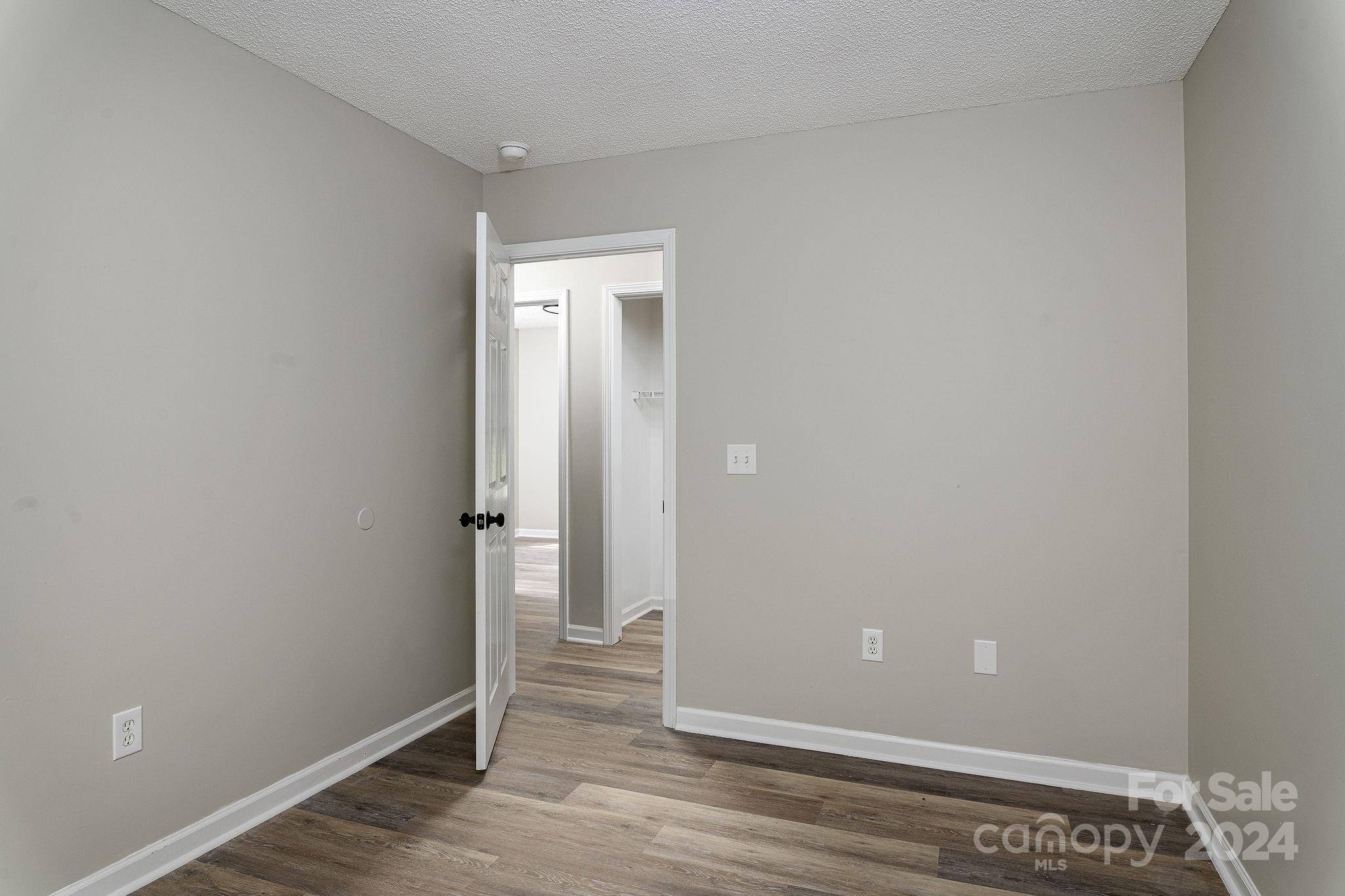 Empty room with gray walls and wood-look flooring, viewed toward an open door and hallway.